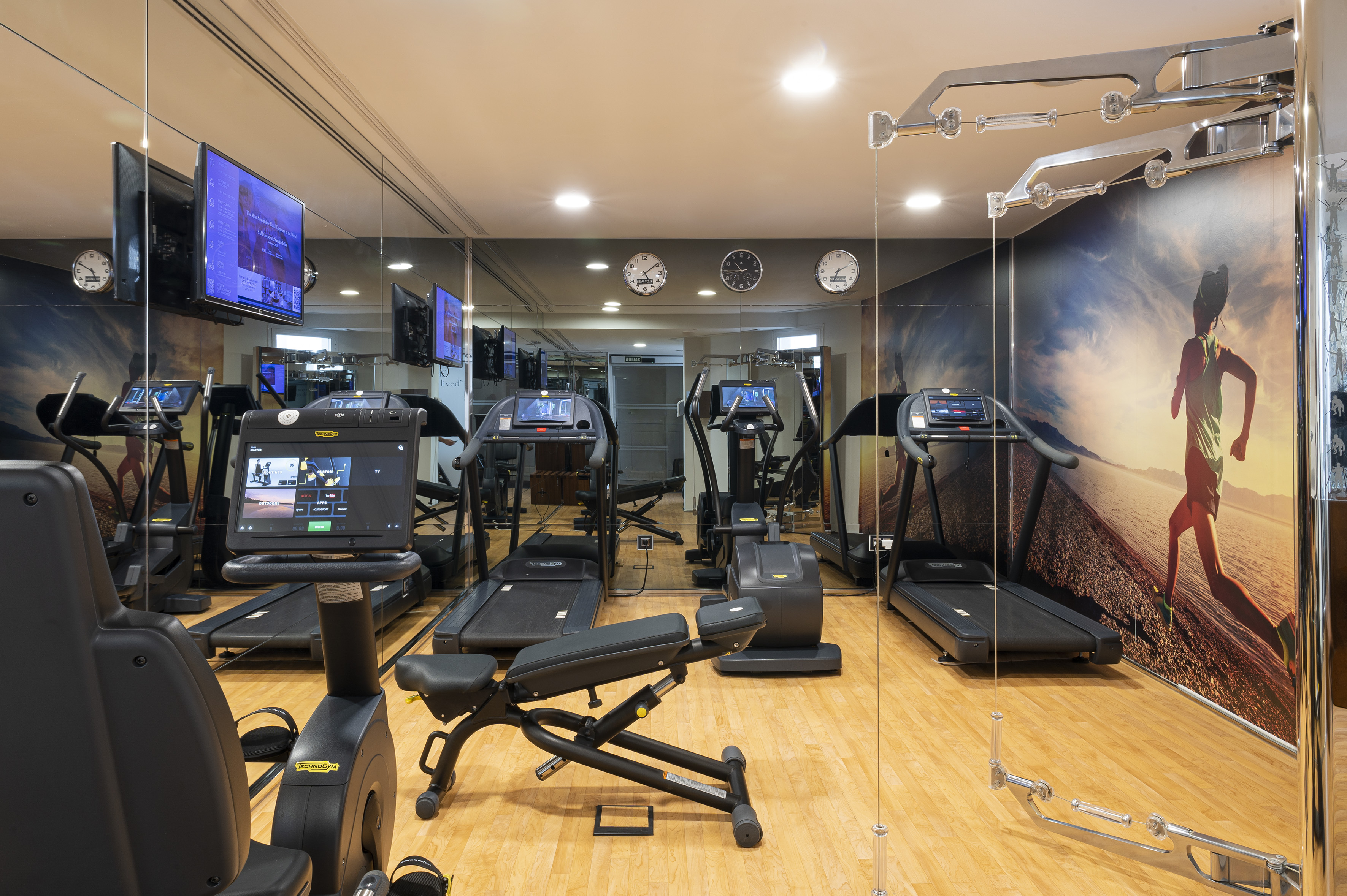 Modern gym with treadmills, fitness equipment, TVs, and mirrored walls.