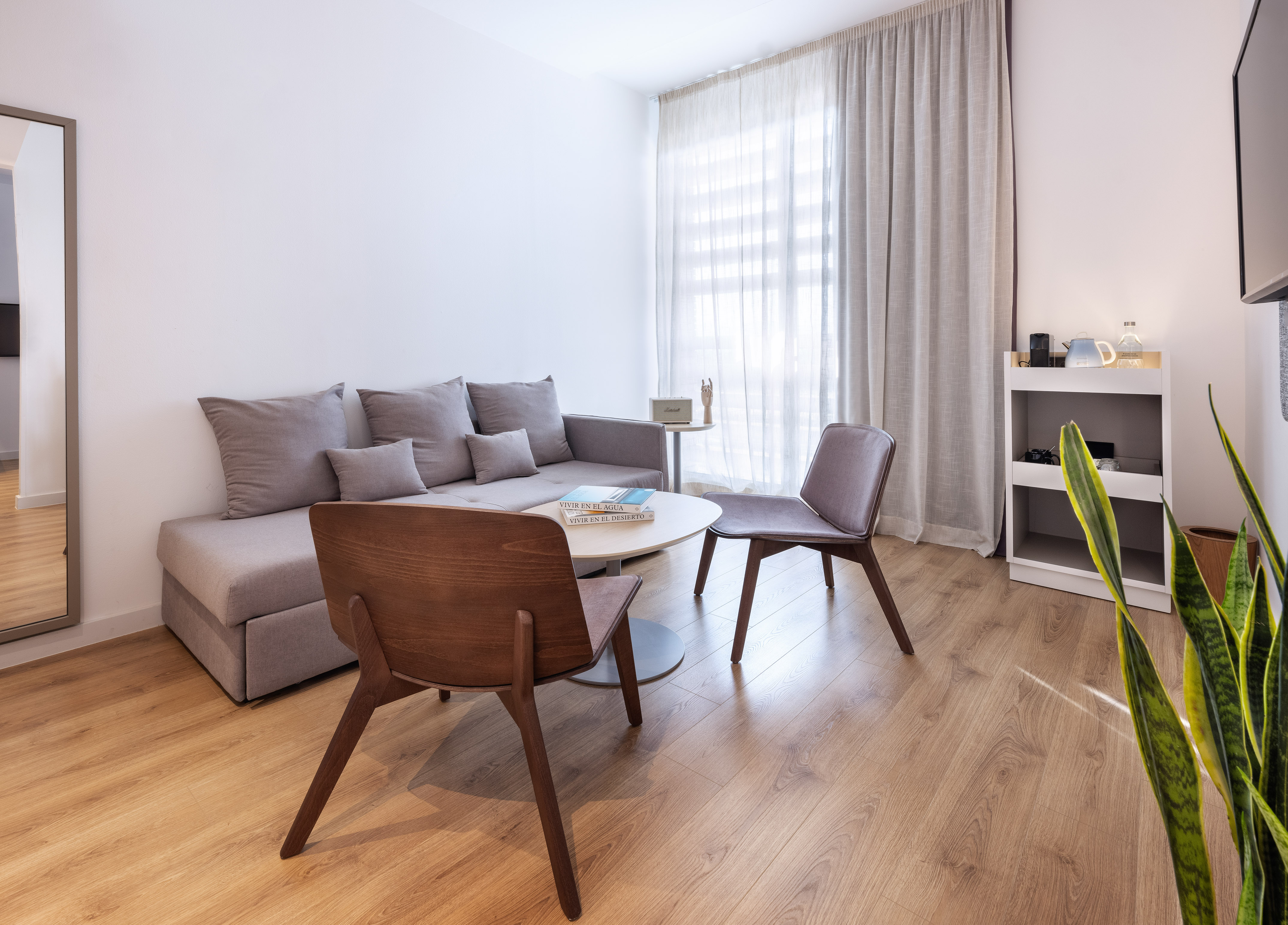 Modern minimalist living room with grey sofa, wooden chairs, coffee table, wood floor.