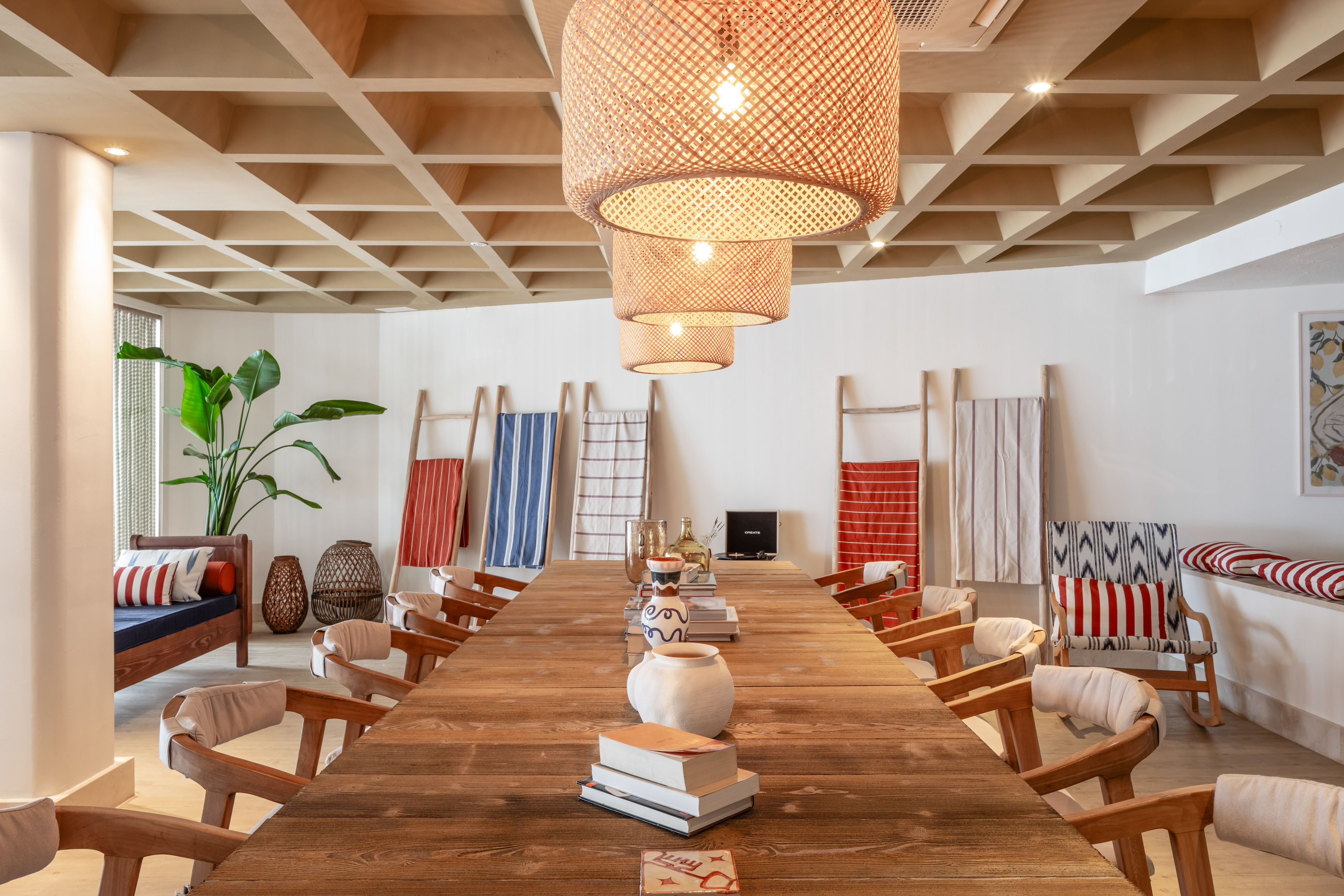 Long wooden communal dining table with rattan pendant lights and natural decor.