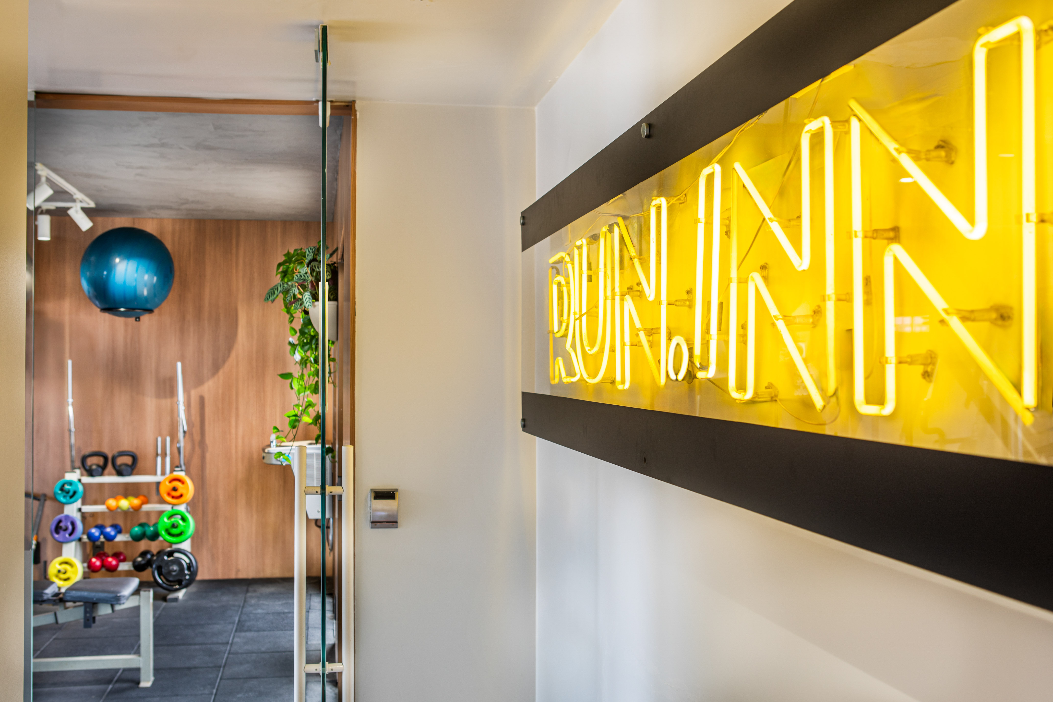 Yellow neon "RUNN" sign alongside home gym: weights, exercise ball.
