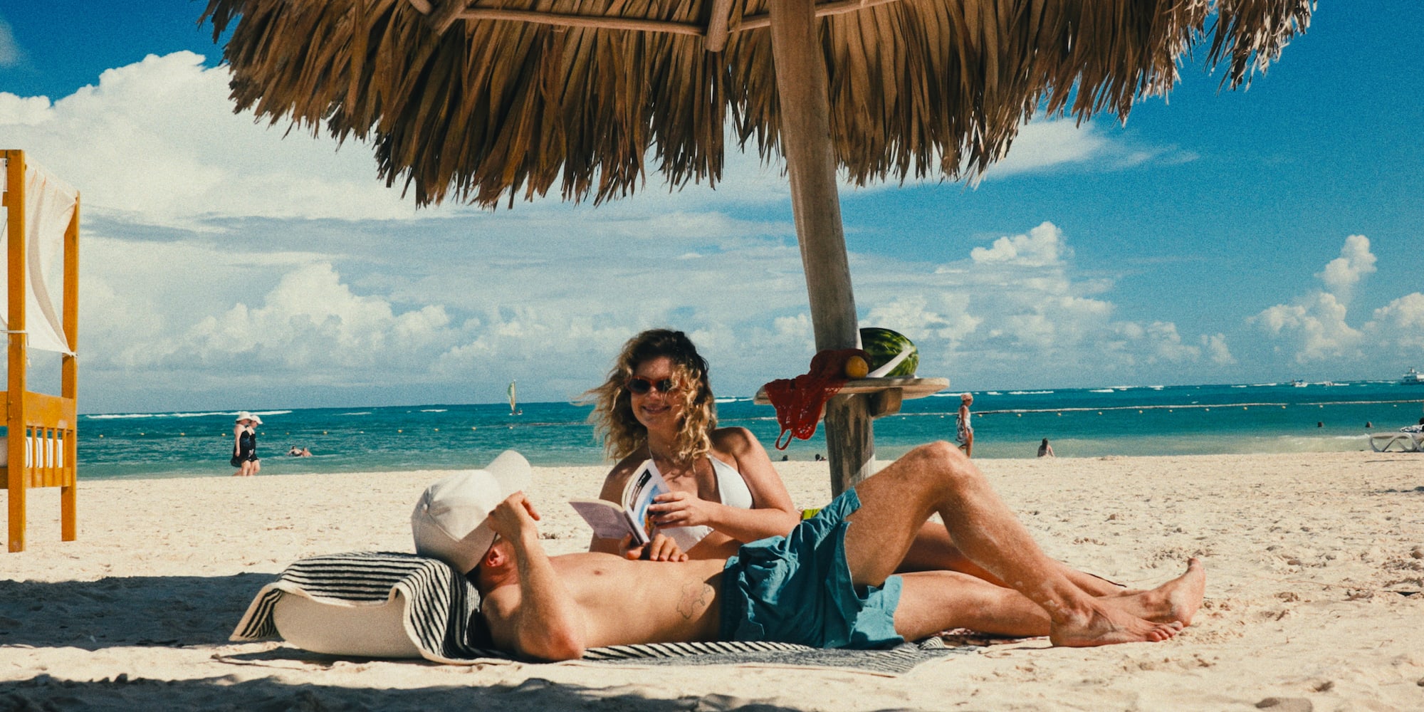 a man and woman lying under a straw umbrella on a beach