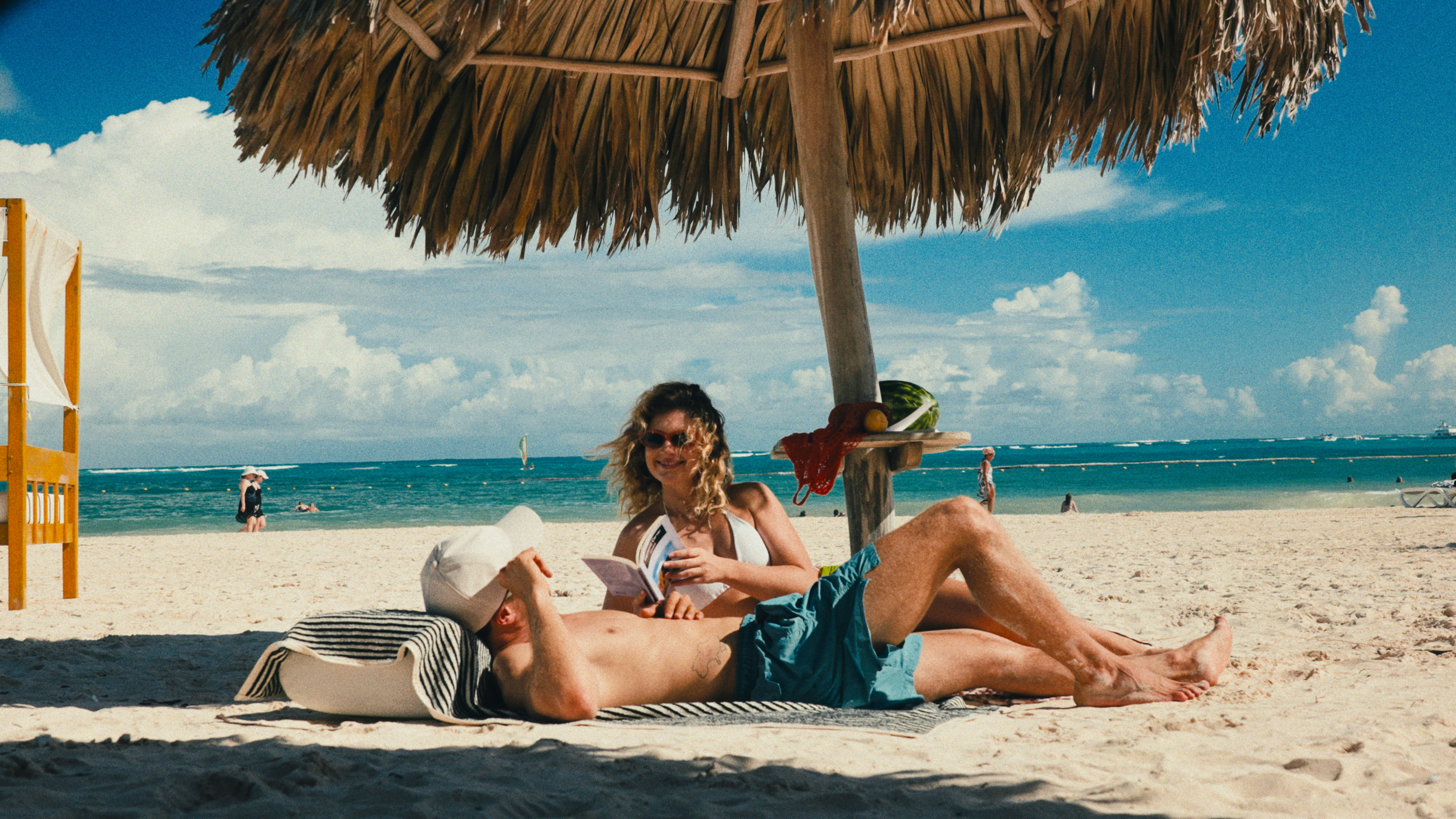 a man and woman lying under a straw umbrella on a beach