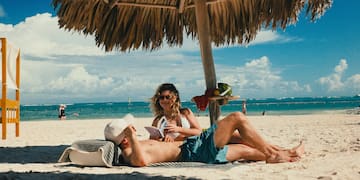 a man and woman lying under a straw umbrella on a beach
