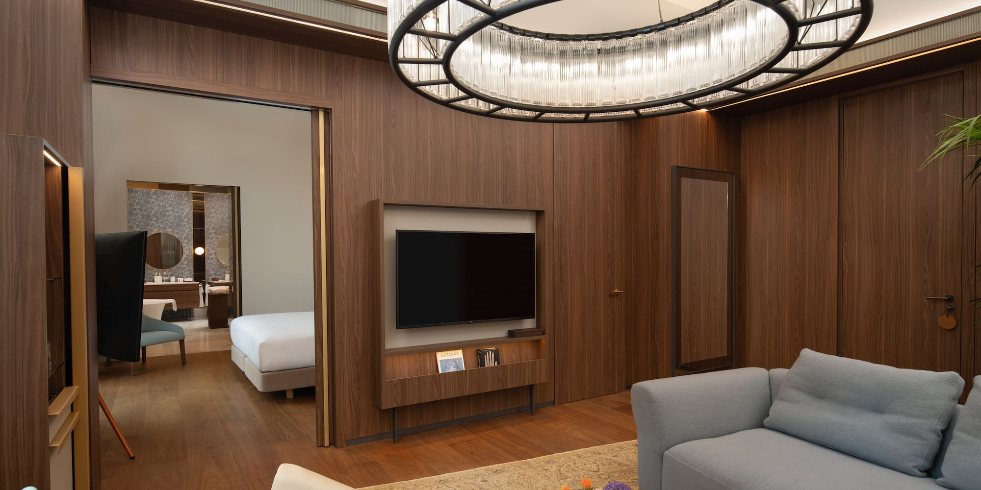 Modern luxury hotel suite living room, wood paneling, elegant chandelier, and bedroom.