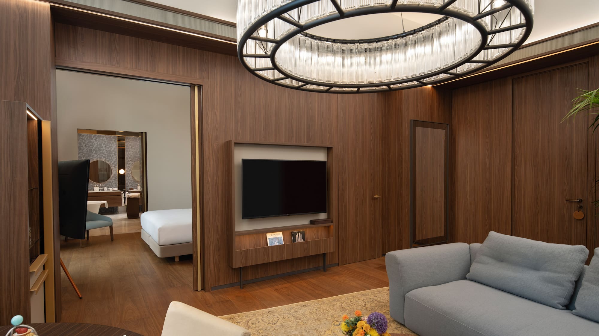 Modern luxury hotel suite living room, wood paneling, elegant chandelier, and bedroom.