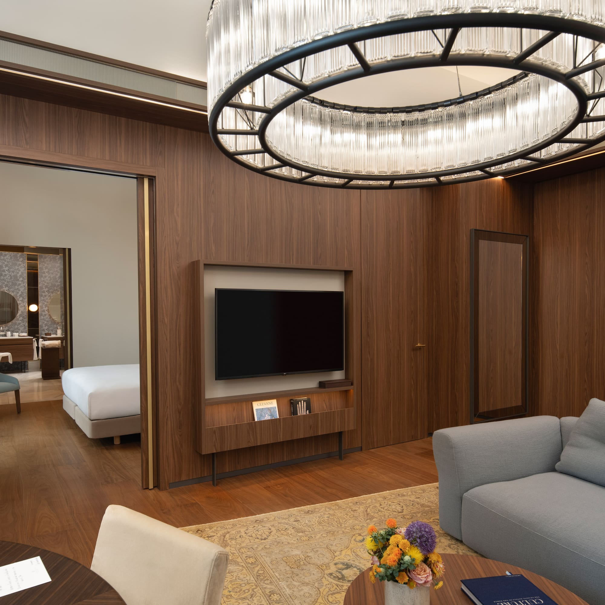 Modern luxury hotel suite living room, wood paneling, elegant chandelier, and bedroom.