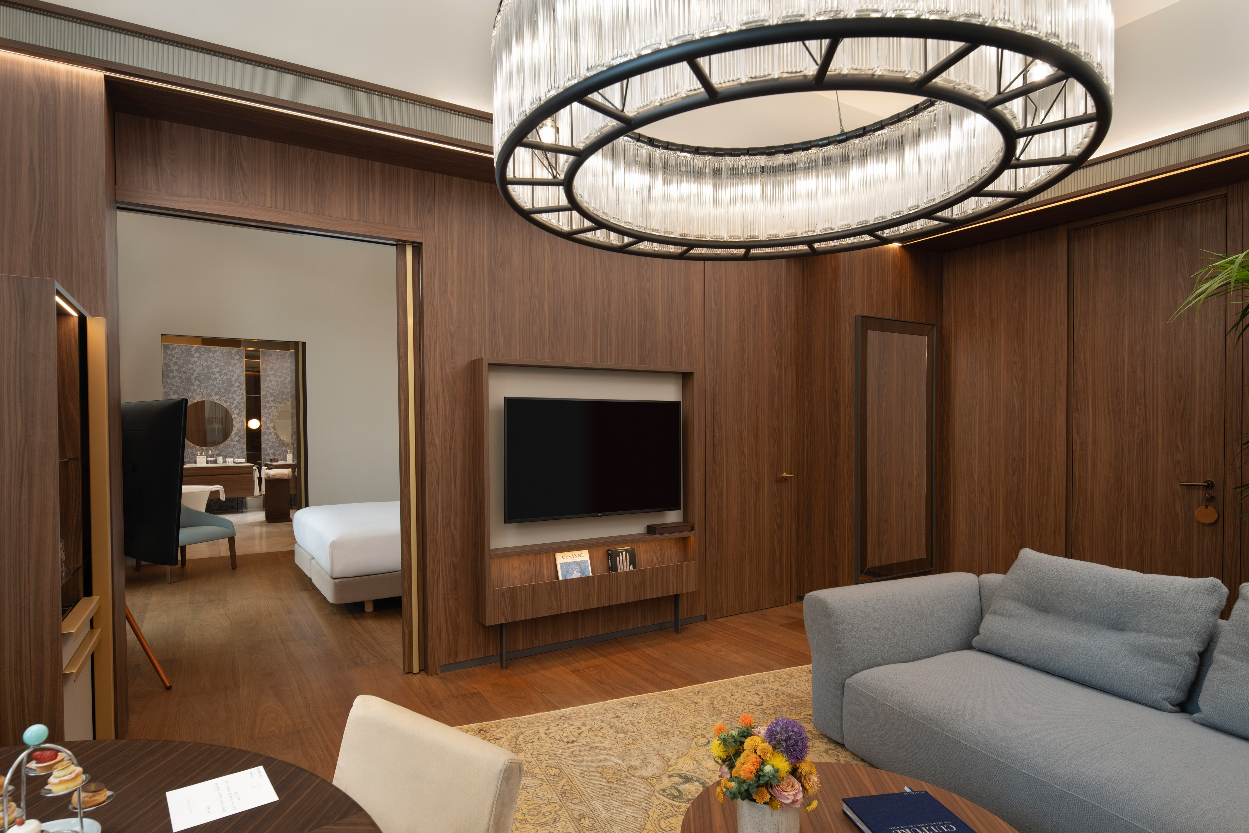 Modern luxury hotel suite living room, wood paneling, elegant chandelier, and bedroom.