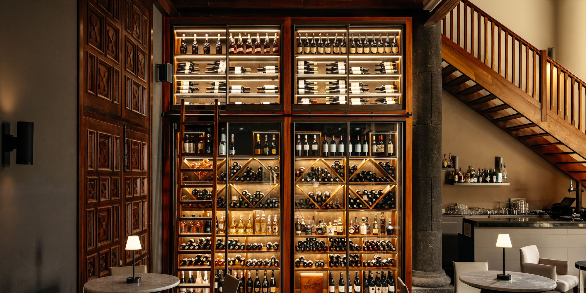 Illuminated wine and spirits display in a restaurant bar area with wooden stairs.