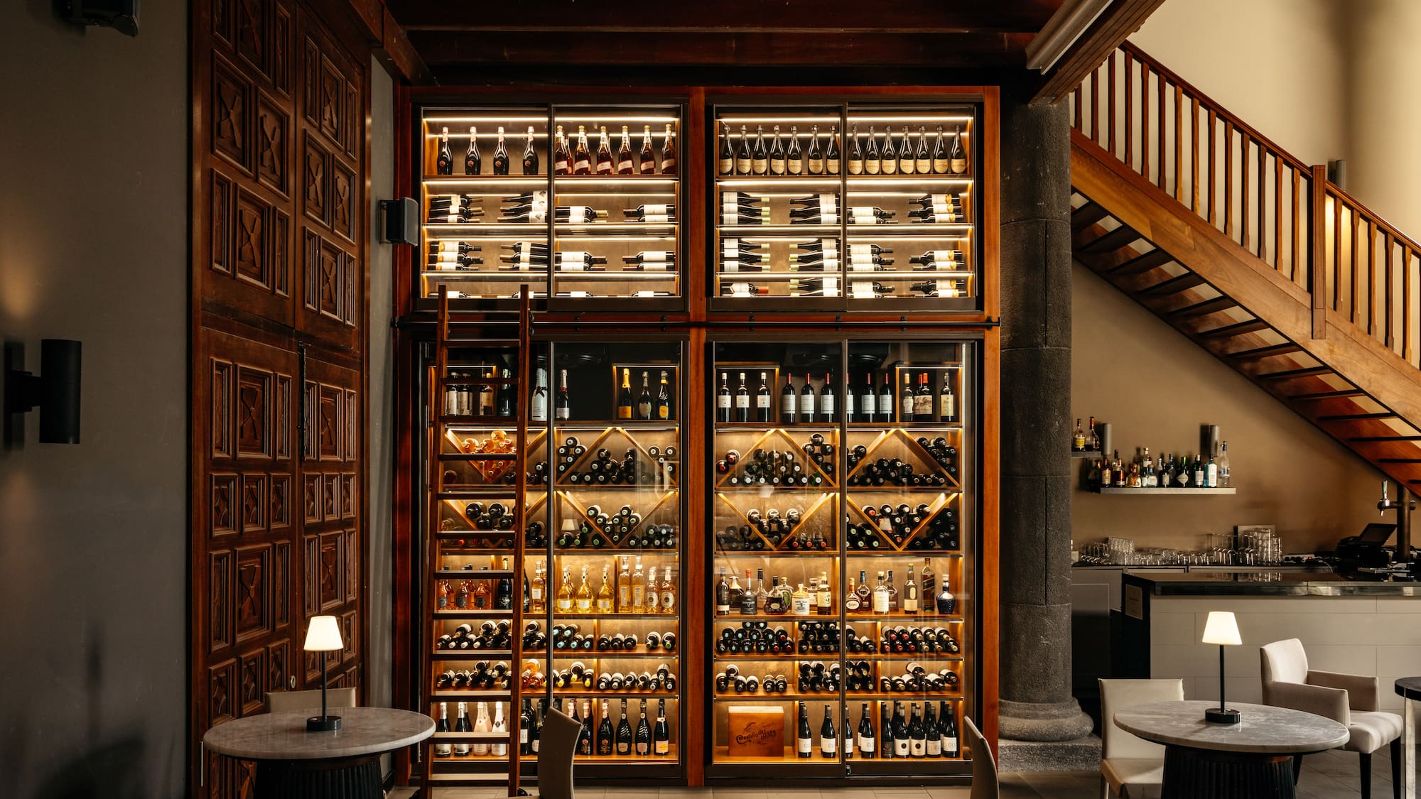 Illuminated wine and spirits display in a restaurant bar area with wooden stairs.