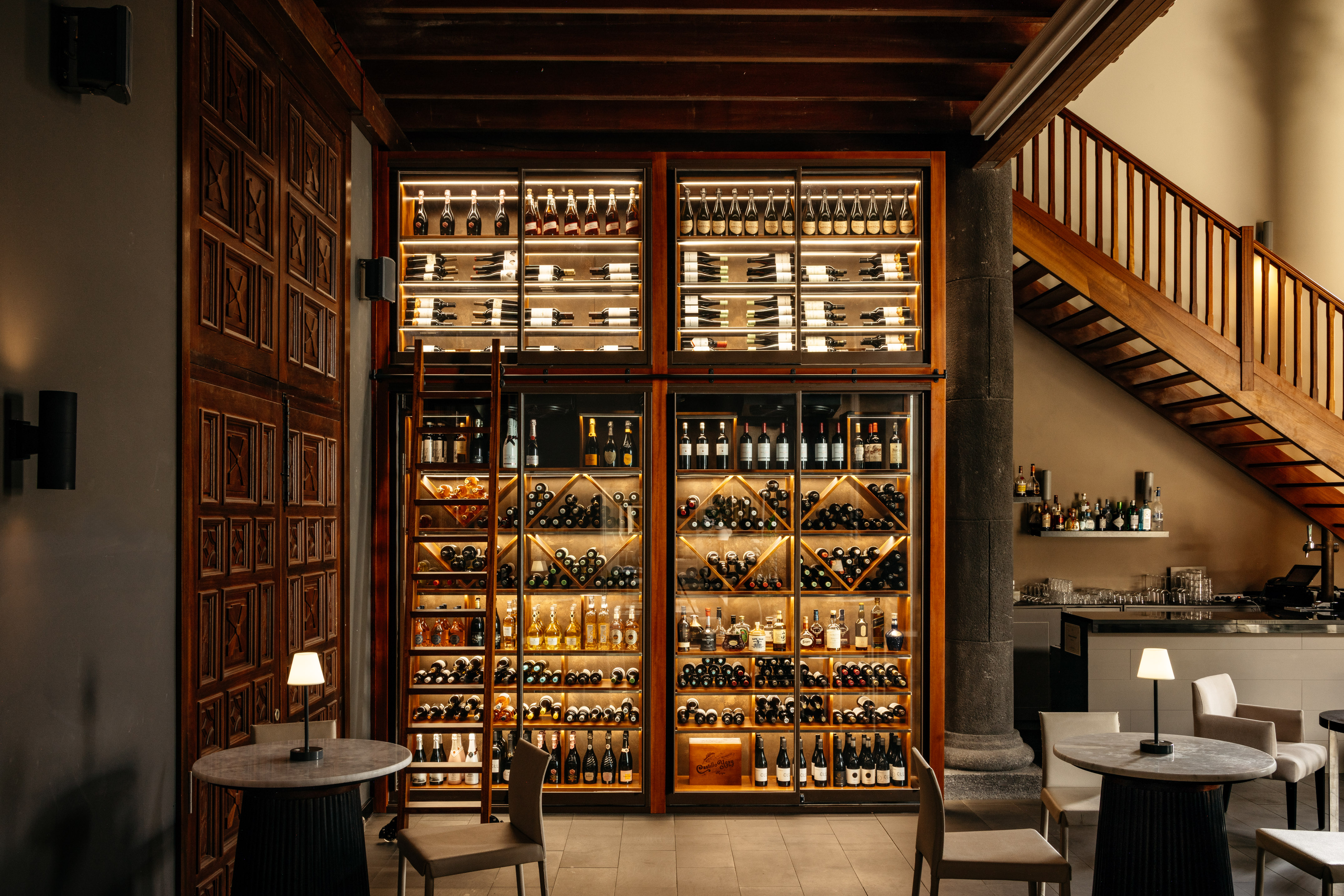 Illuminated wine and spirits display in a restaurant bar area with wooden stairs.
