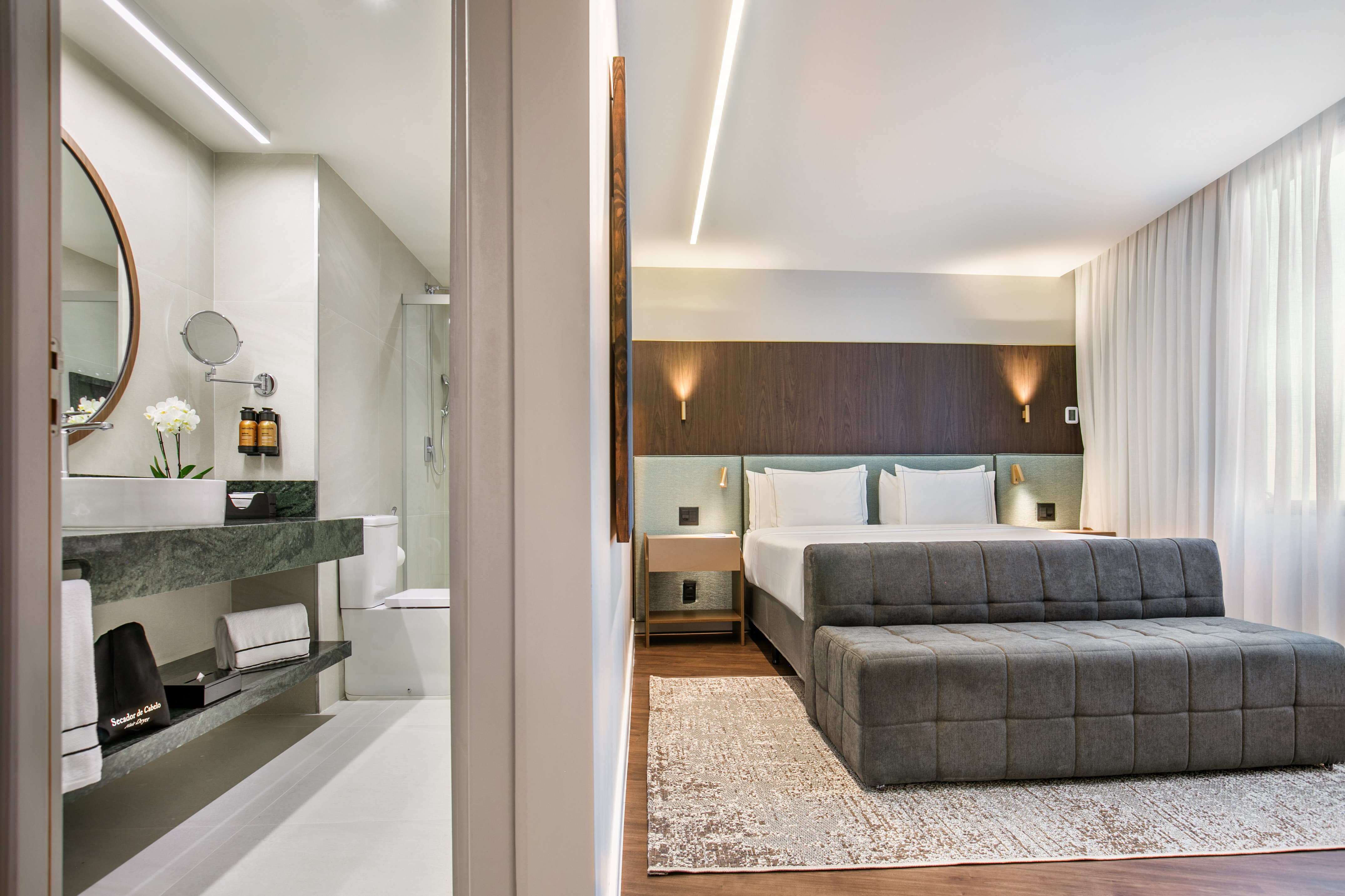 Modern hotel room: bed, sofa, wood floor, and bathroom with marble vanity.