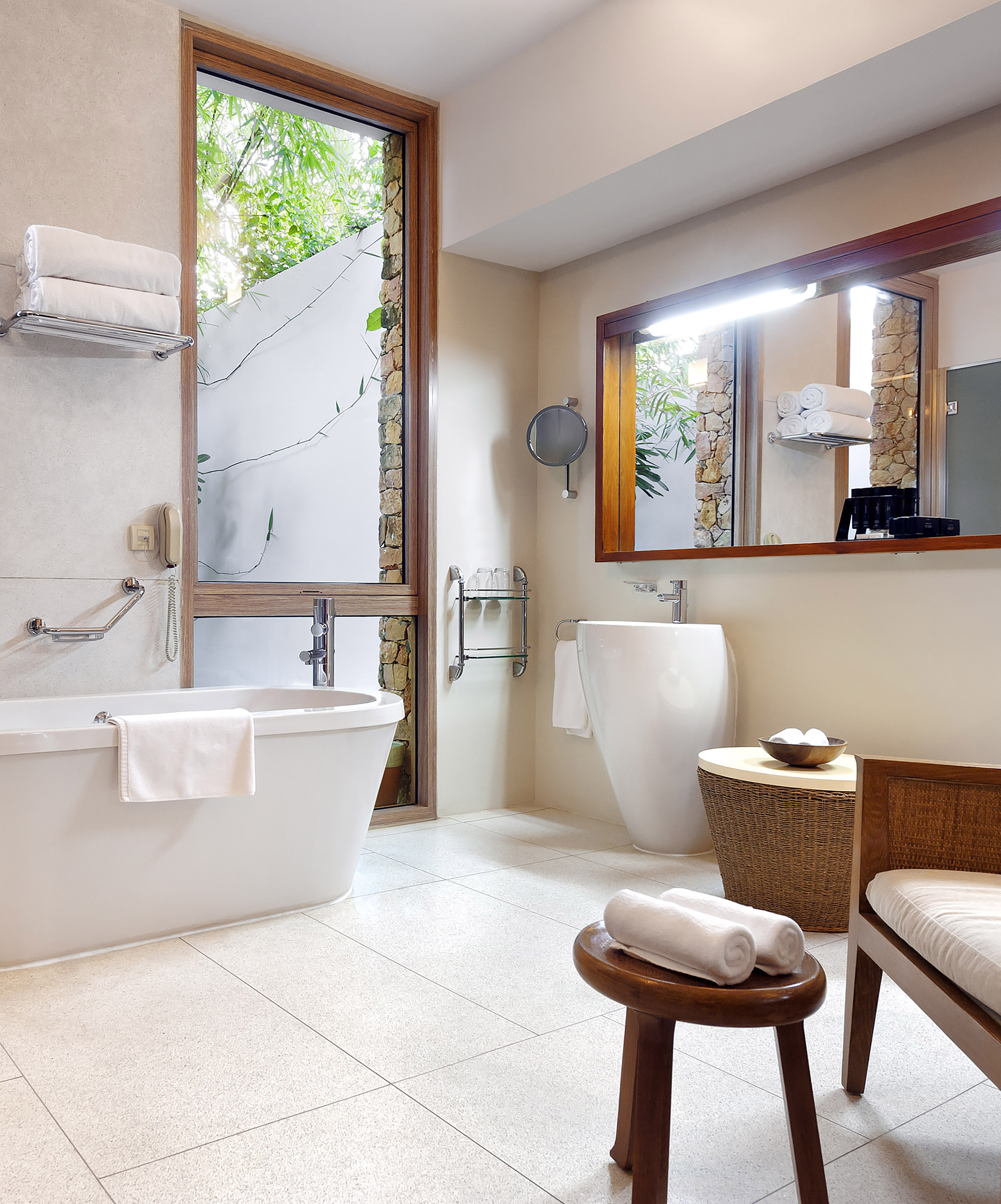 Modern spa bathroom with freestanding tub and tropical window view.