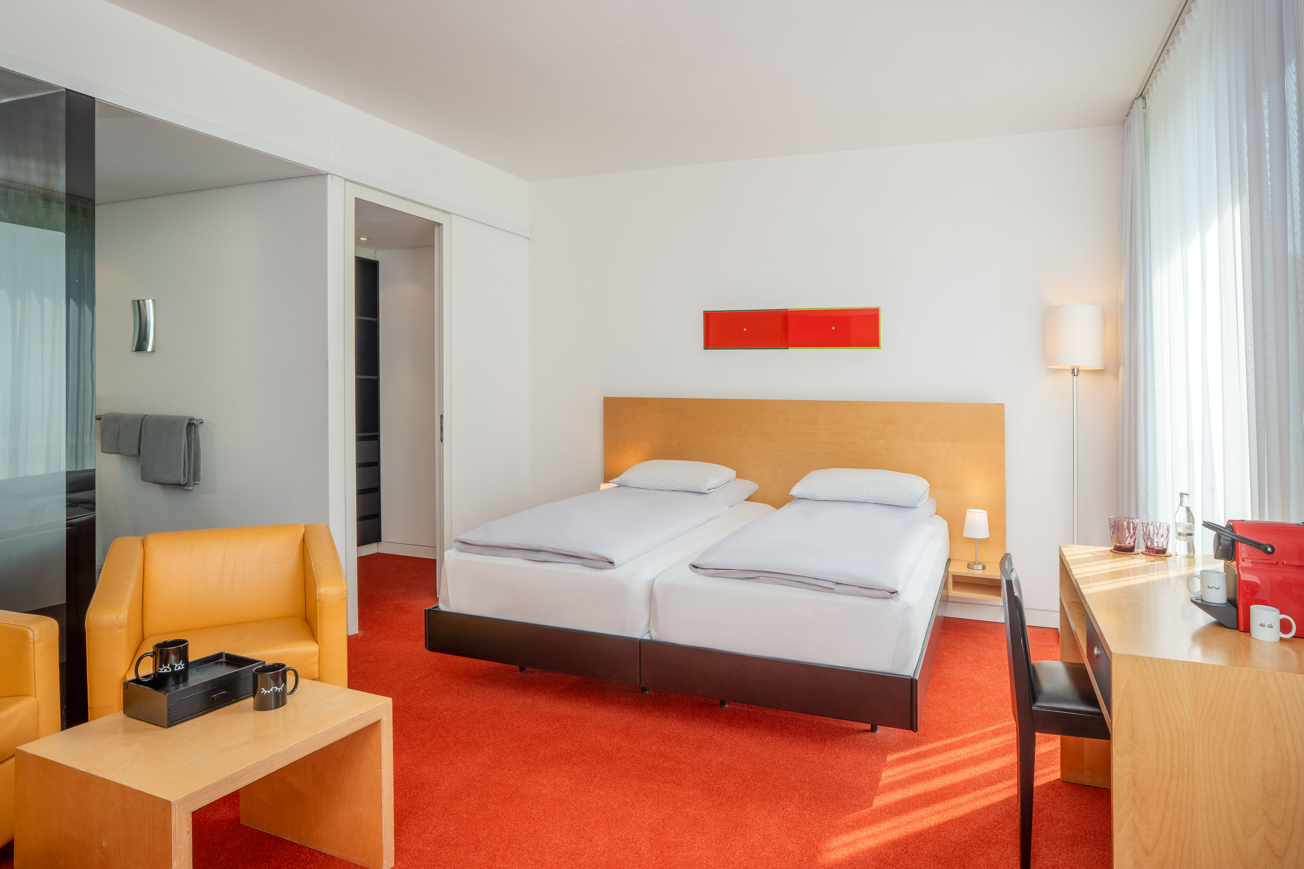 Bright hotel room featuring twin beds, vibrant orange carpet, and modern decor.