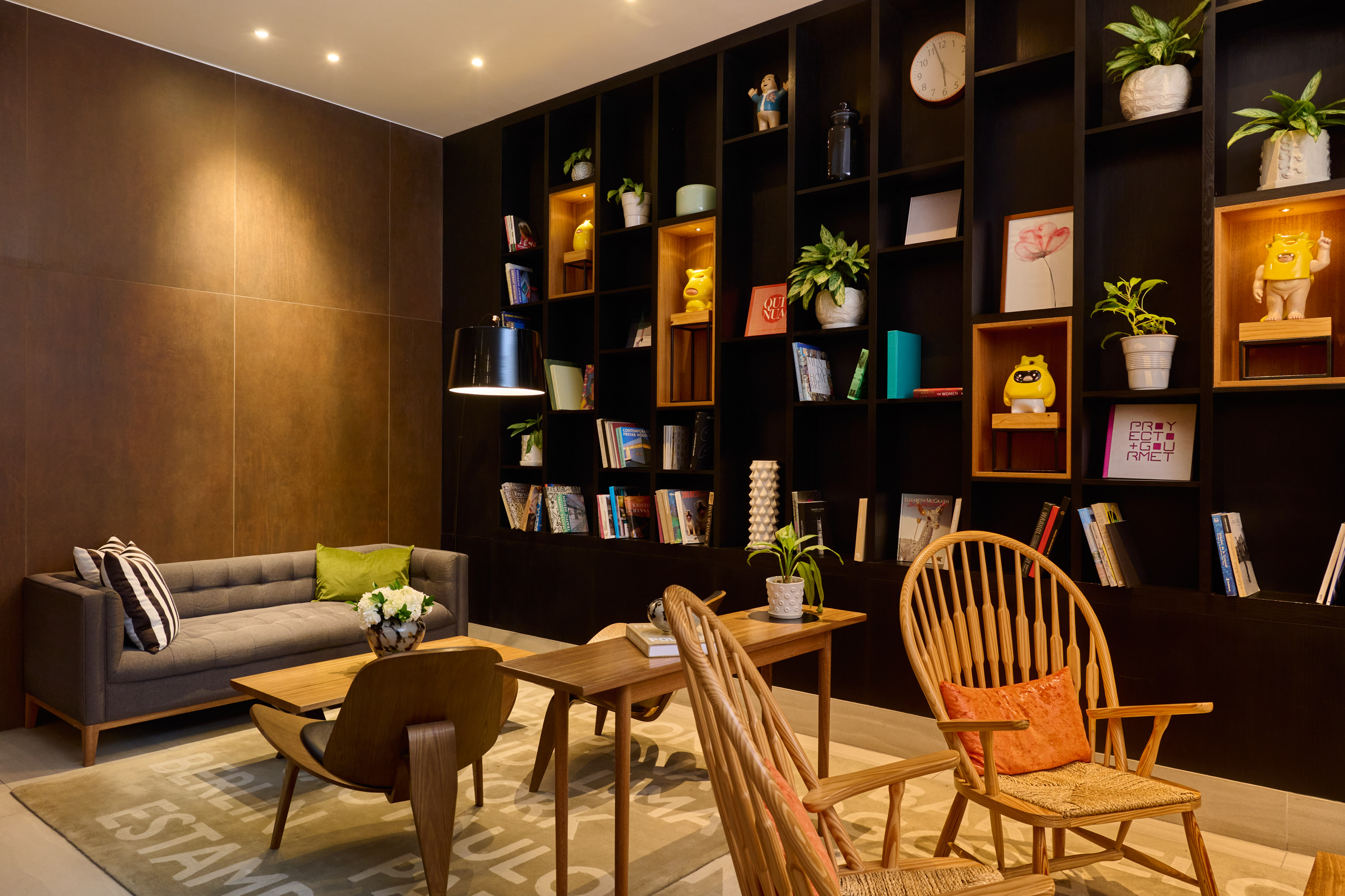 Modern lounge with gray sofa, wooden chairs, and dark built-in bookshelf.