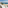 Modern balcony overlooking sunny beach, turquoise ocean, coastal resort buildings.