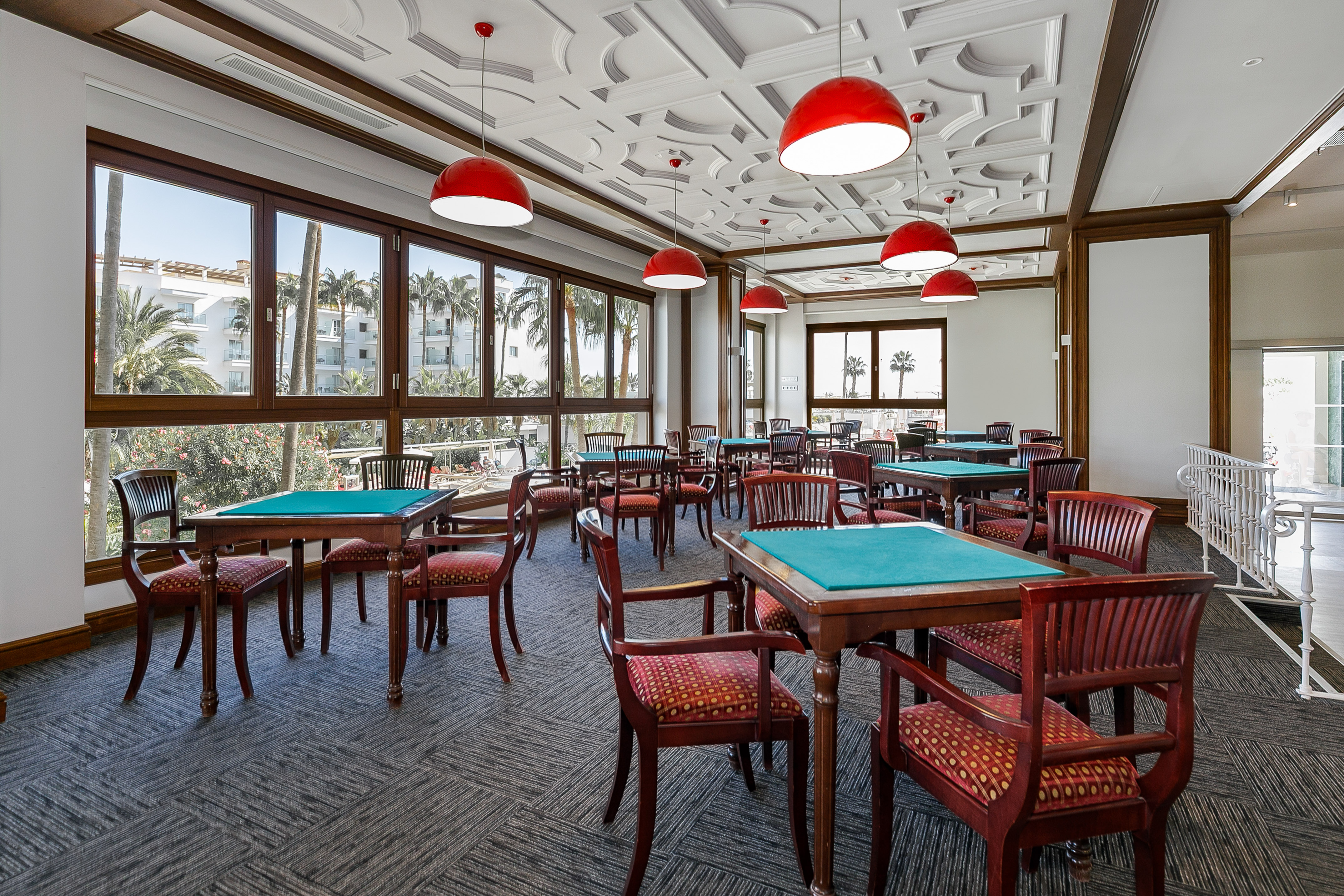 Elegant game room with card tables, red pendant lights, and palm tree views.