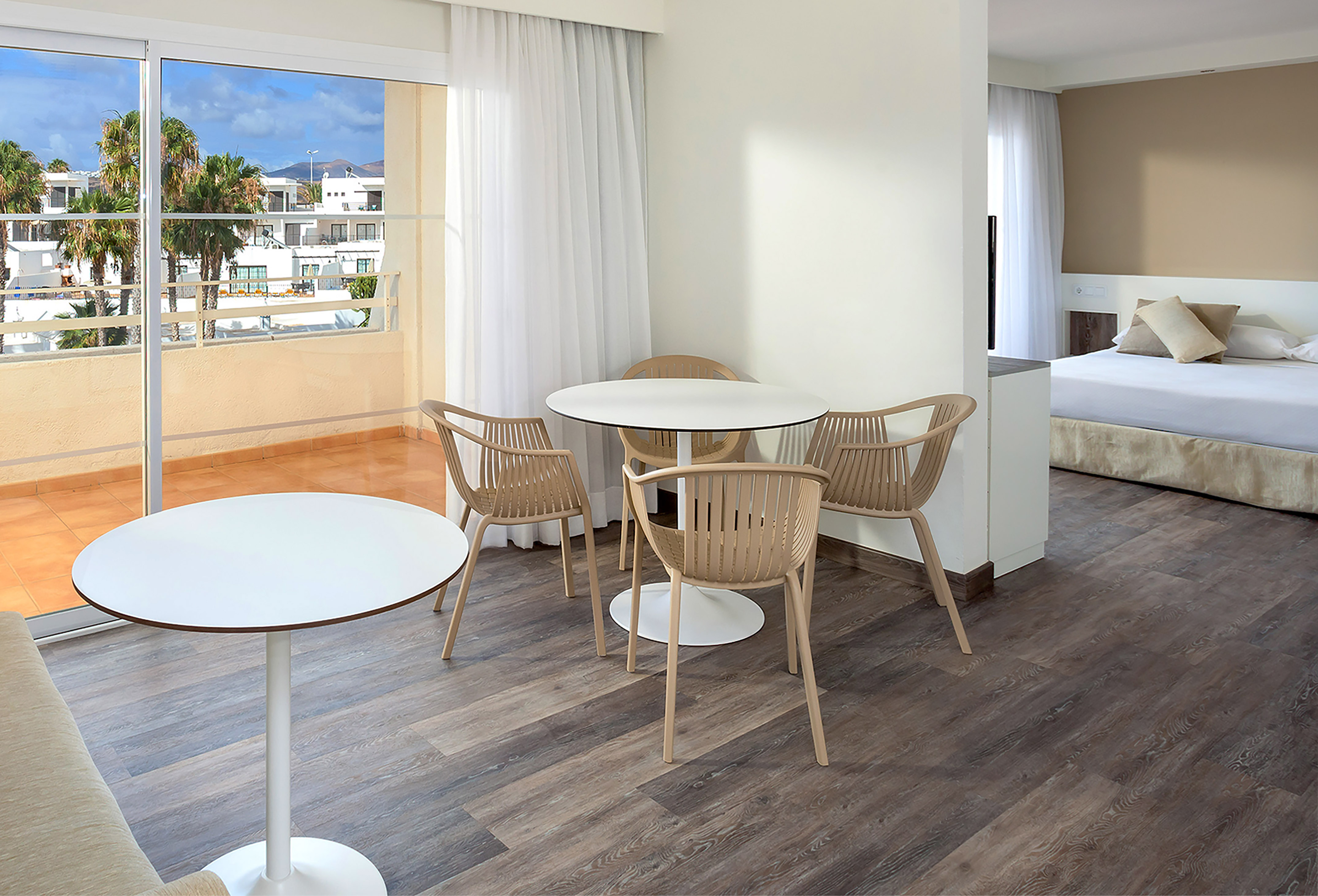 Modern hotel apartment with dining area, bedroom, and balcony view of palm trees.