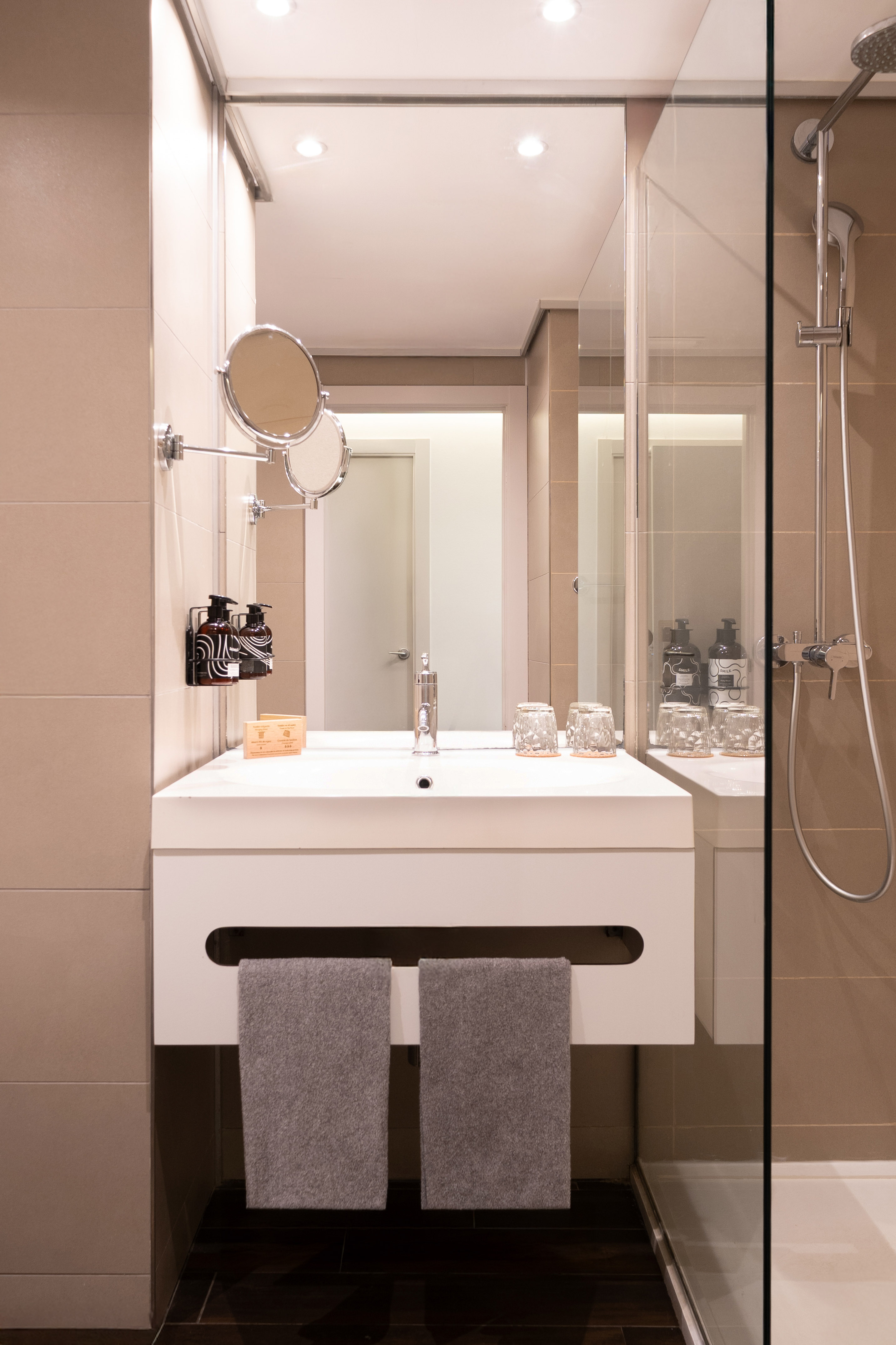 Modern bathroom with white vanity sink, large mirror, glass shower, grey towels.