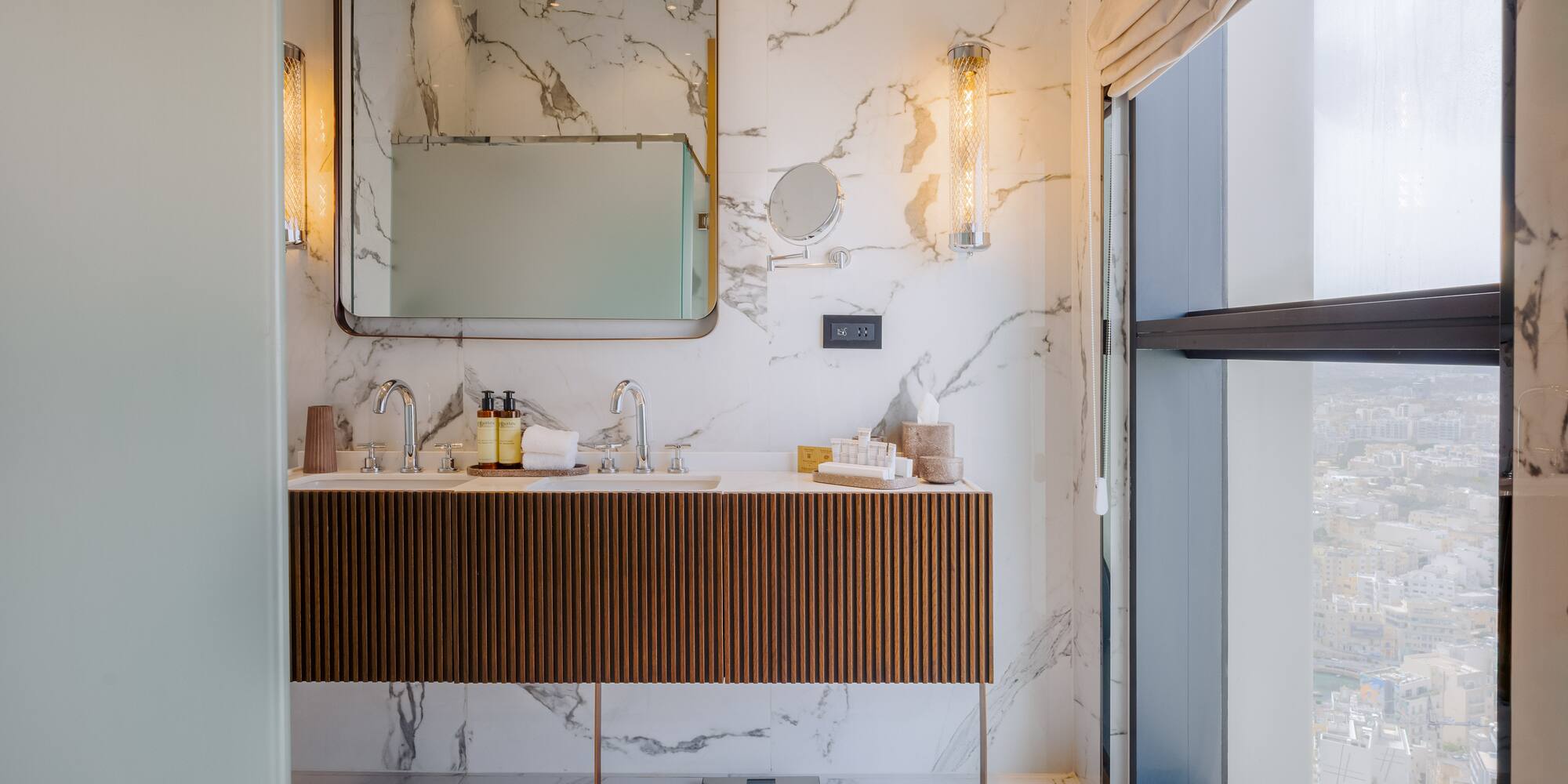 Luxury marble bathroom with double vanity, modern design, and city view from window.
