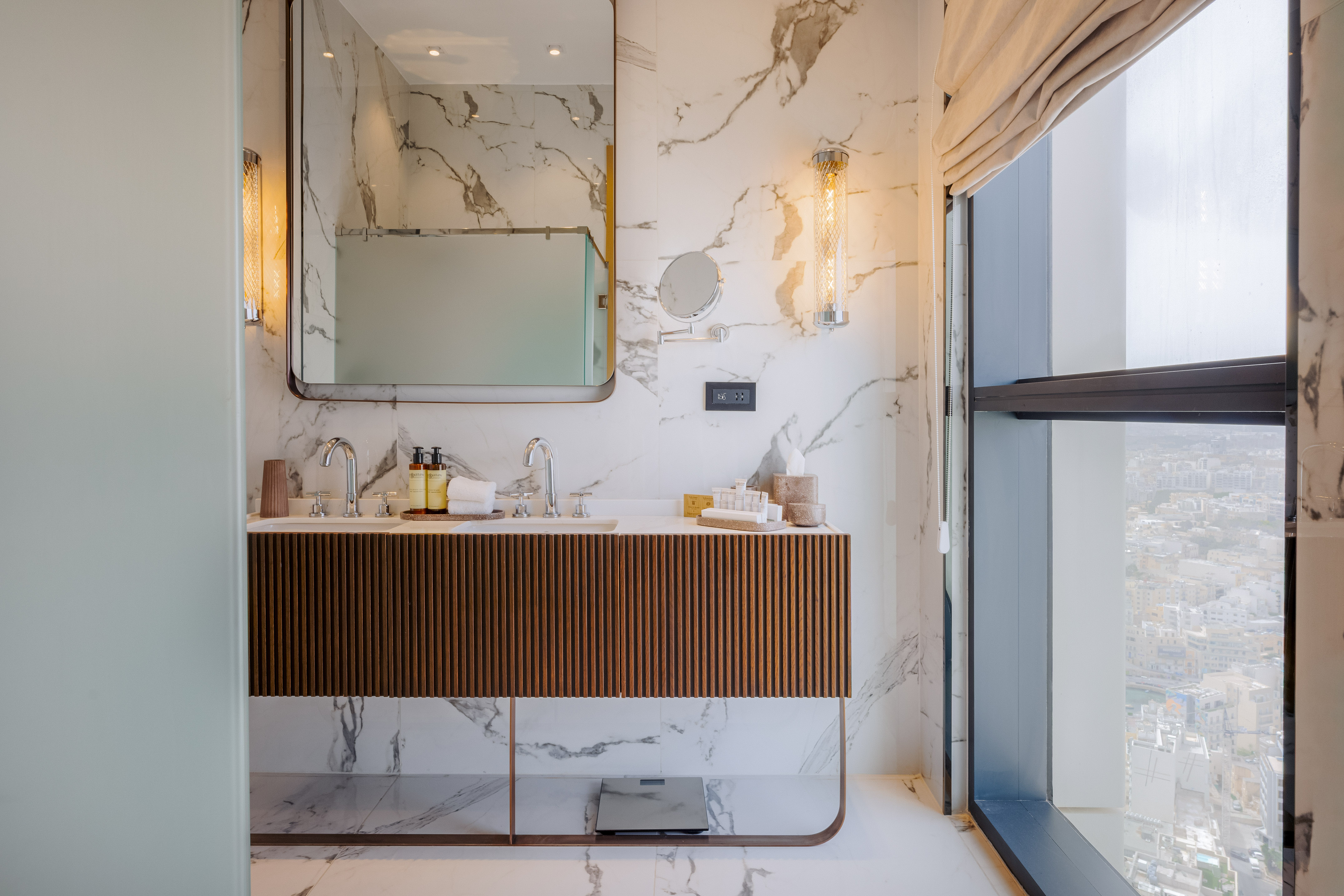 Luxury marble bathroom with double vanity, modern design, and city view from window.