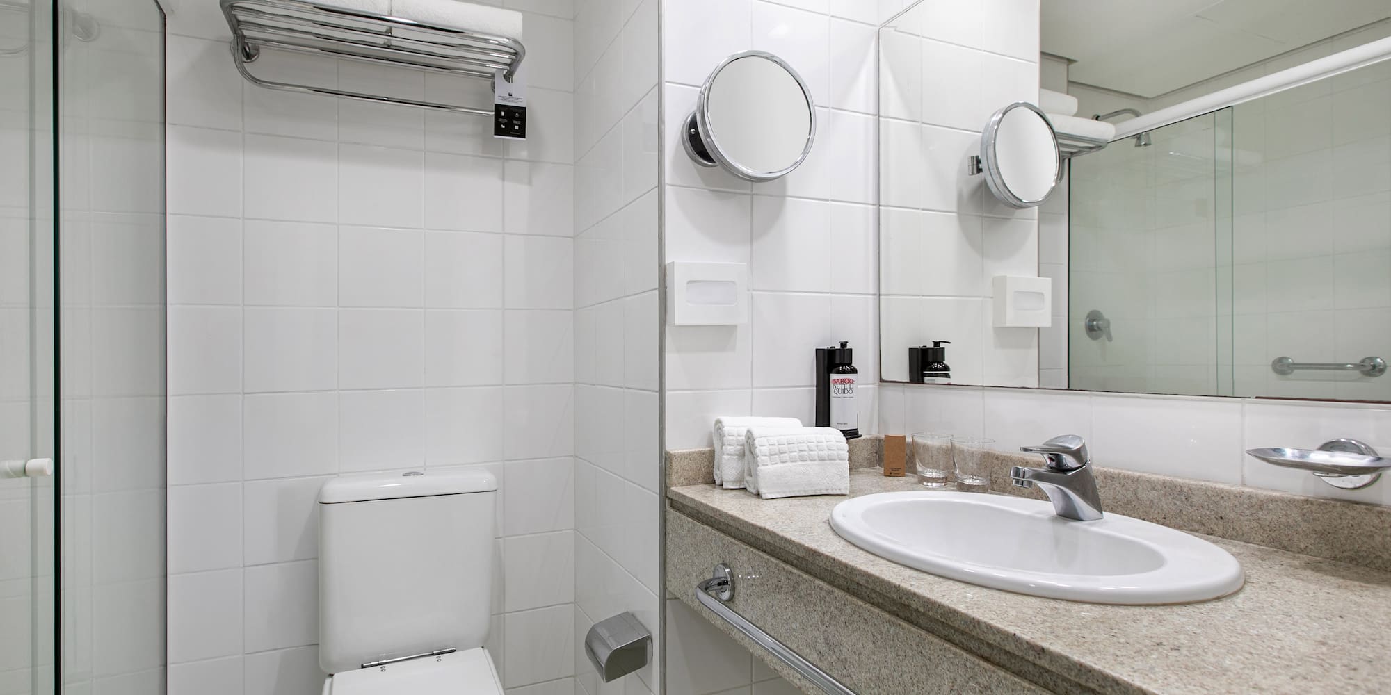 Modern white hotel bathroom with toilet, sink vanity, shower, and fresh towels.