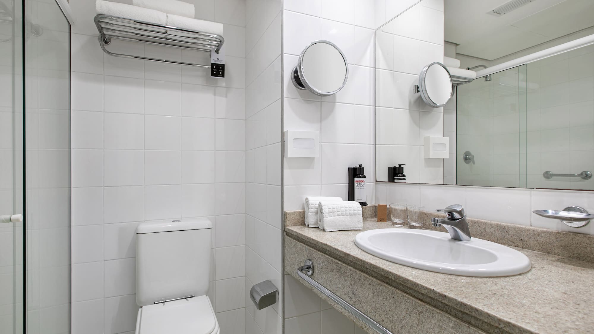 Modern white hotel bathroom with toilet, sink vanity, shower, and fresh towels.