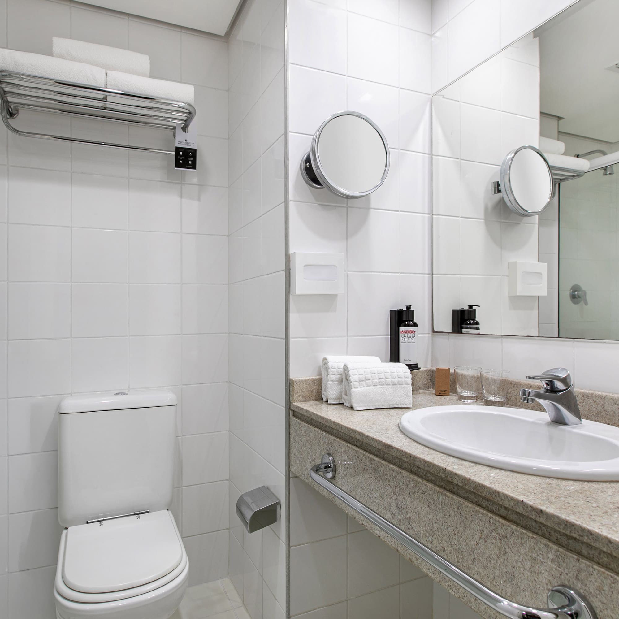 Modern white hotel bathroom with toilet, sink vanity, shower, and fresh towels.