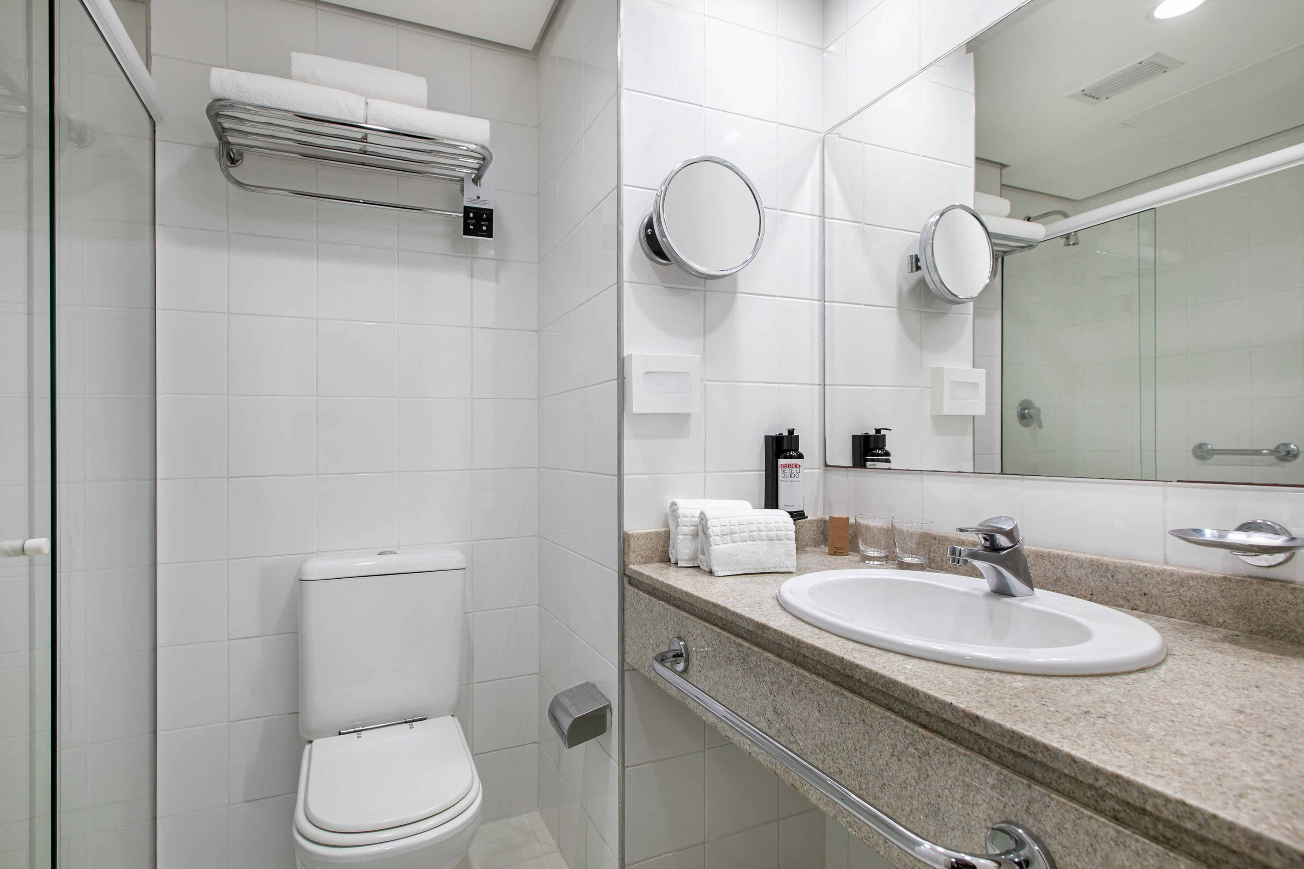 Modern white hotel bathroom with toilet, sink vanity, shower, and fresh towels.