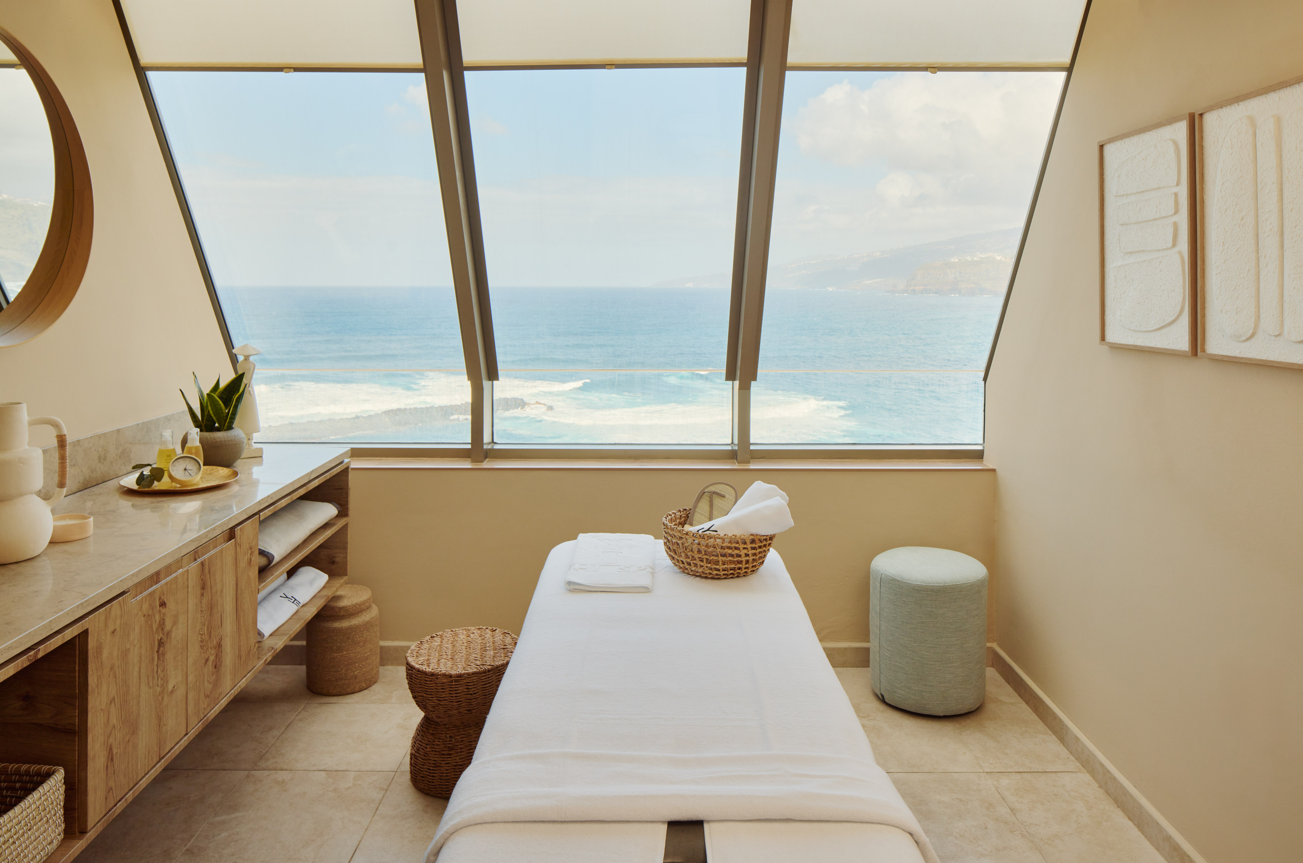 Coastal spa massage room with ocean view, treatment table, and natural decor.