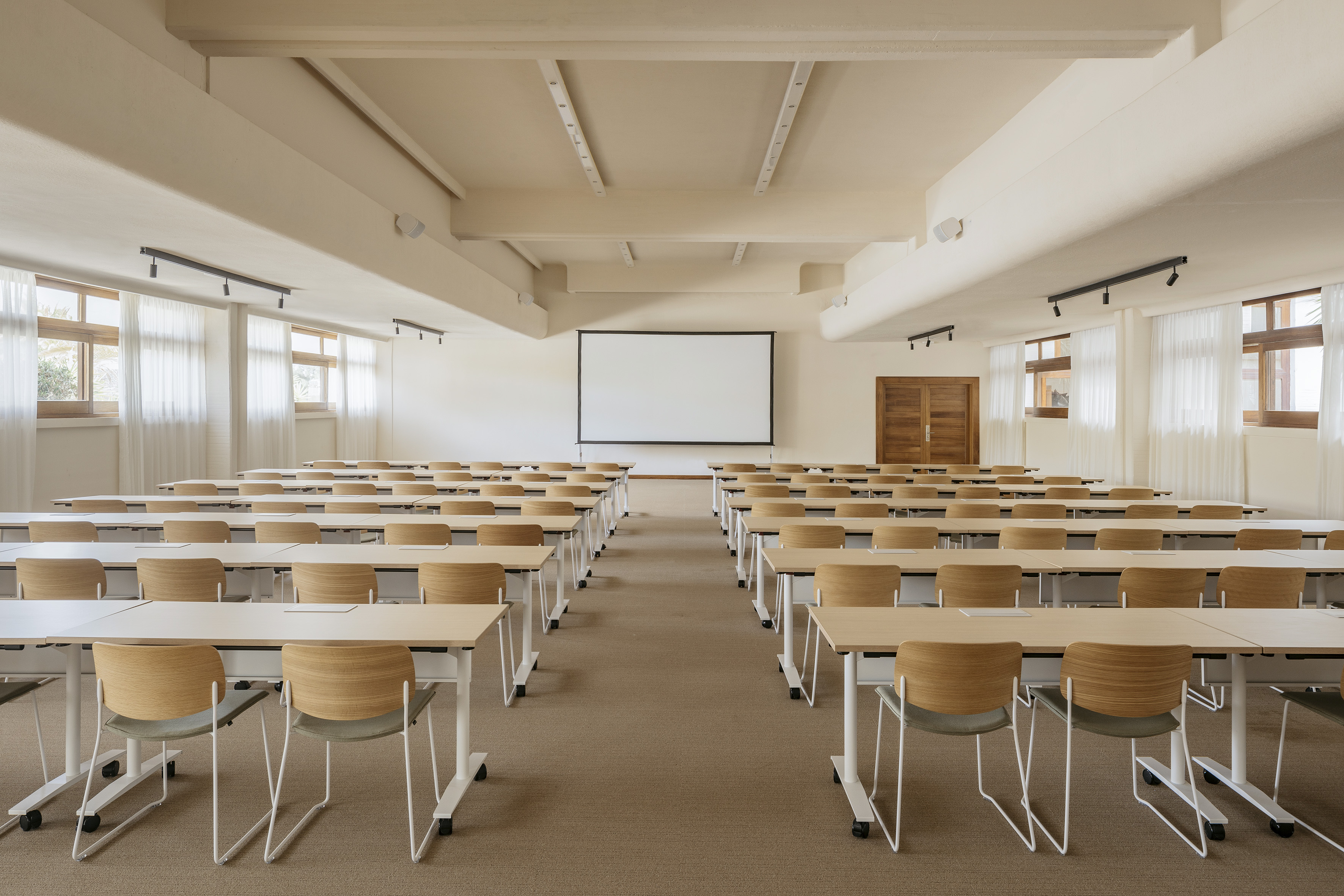 Modern classroom with rows of tables, chairs, and a large projection screen.