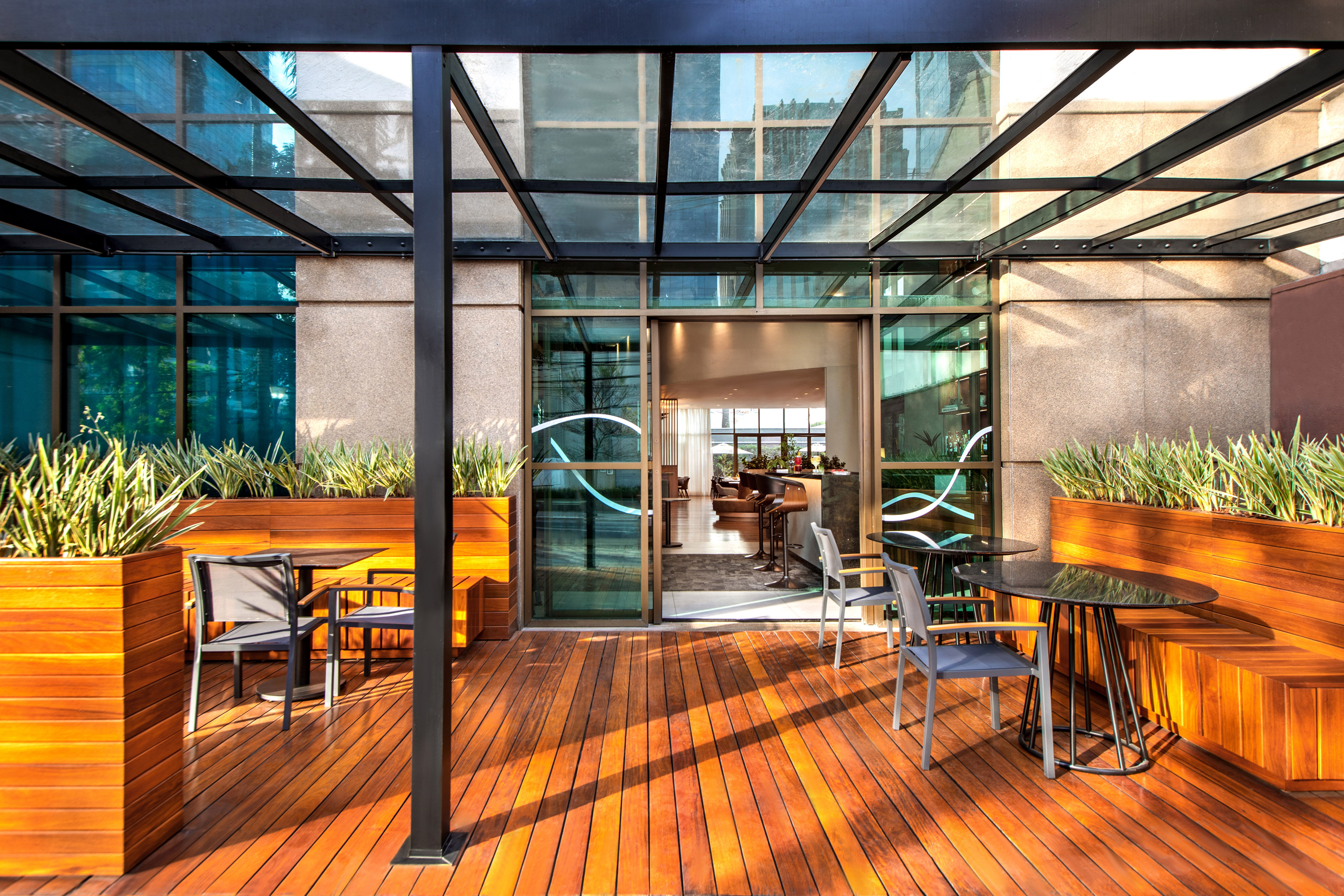 Wooden deck patio with glass canopy, outdoor seating, and lounge entrance.