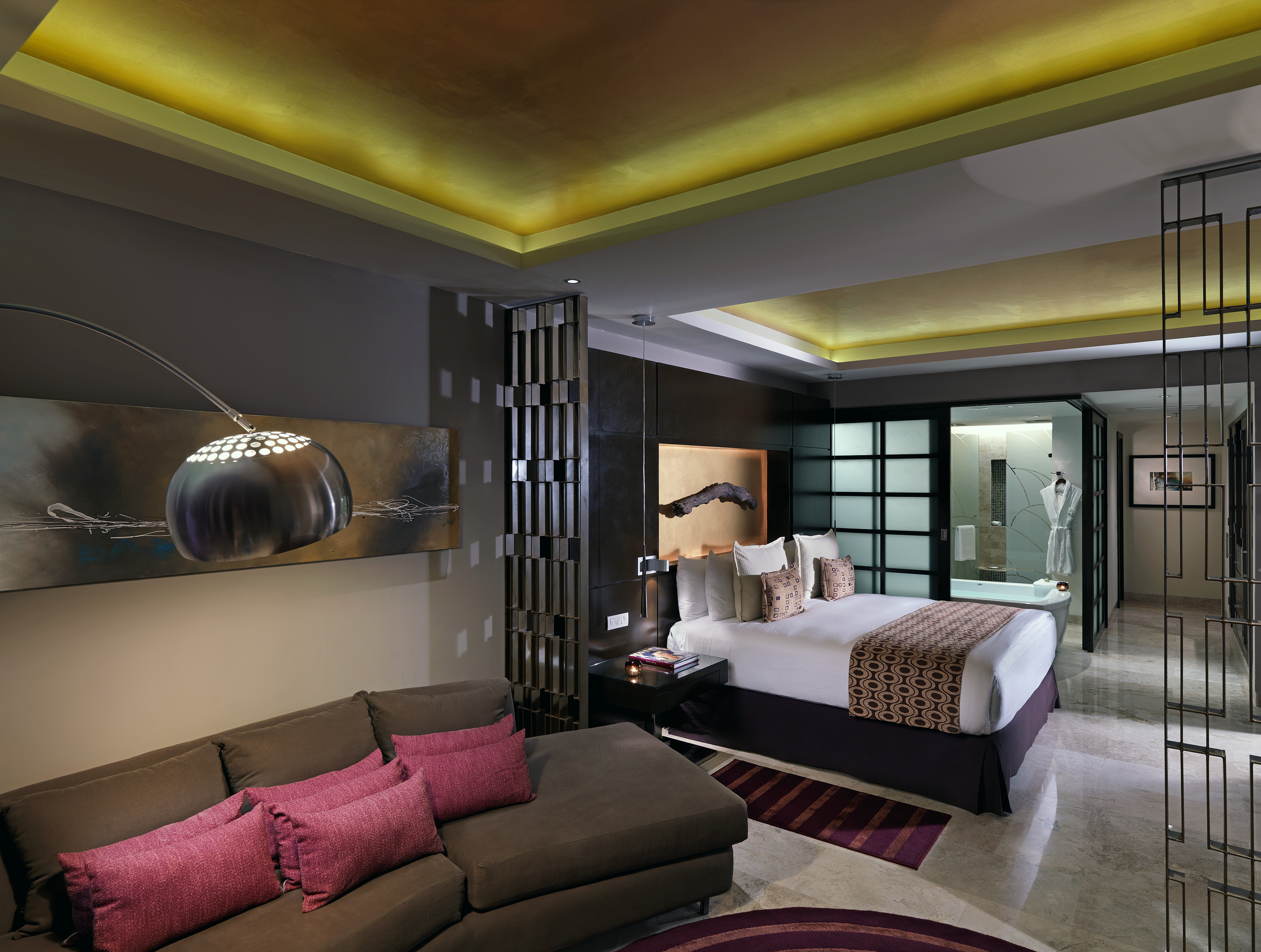 Luxury modern bedroom suite with king bed, sofa, gold lighting, and open bath.