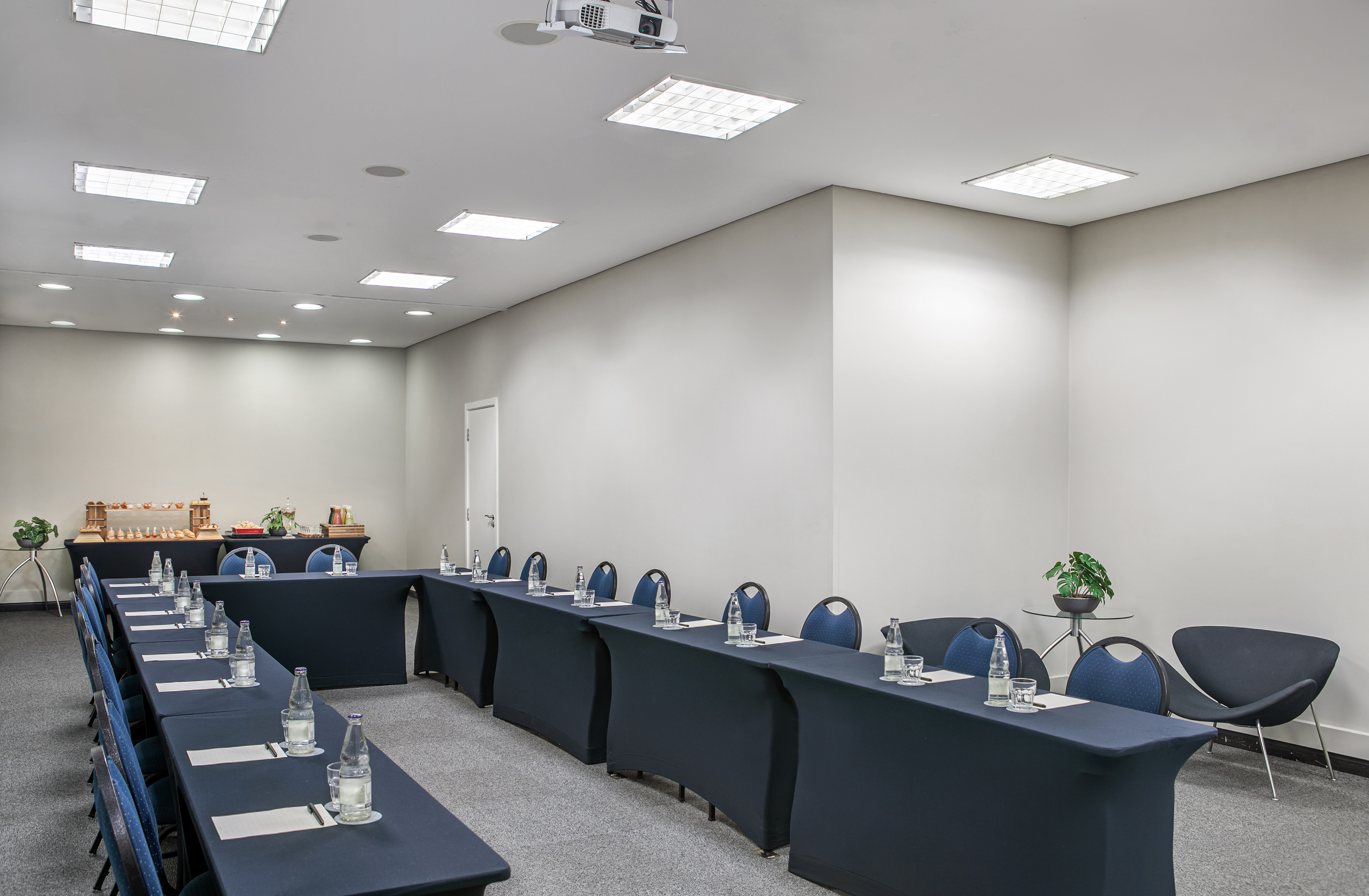 U-shaped conference room with projector, blue tables, chairs, and buffet.