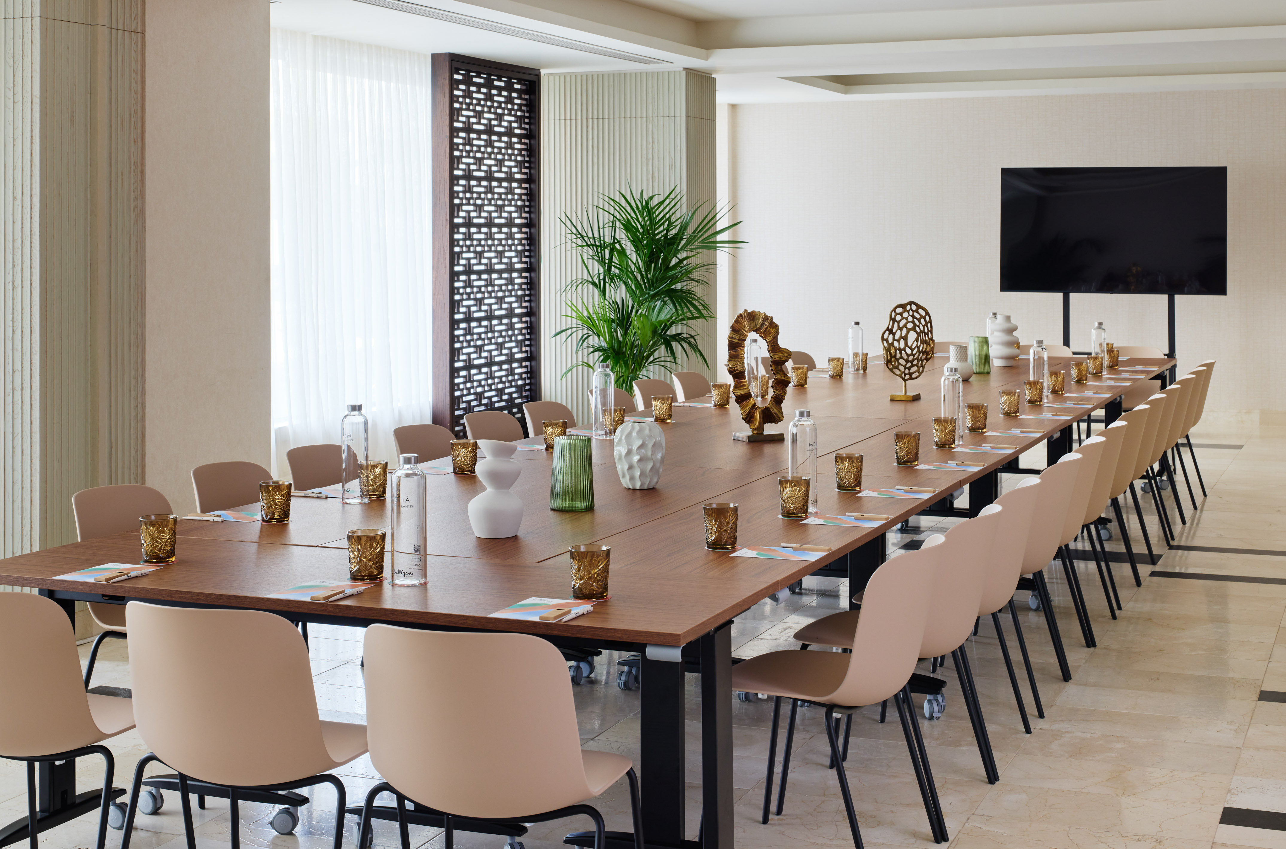 Modern conference room with long table, beige chairs, and large TV.