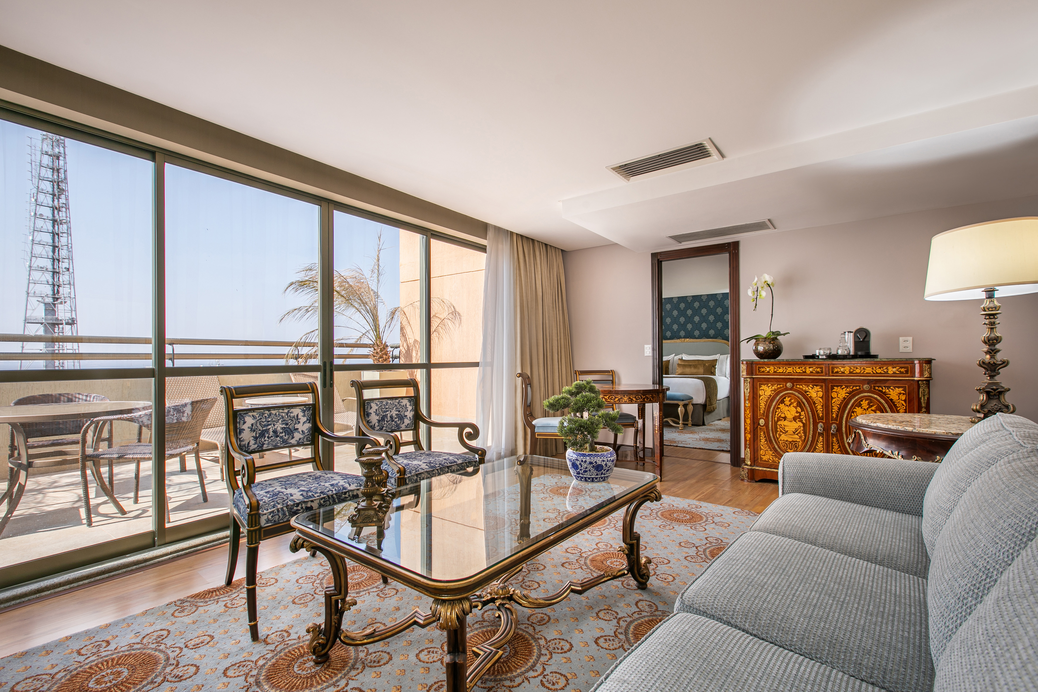 Elegant hotel suite living room with balcony, ocean view, and ornate decor.