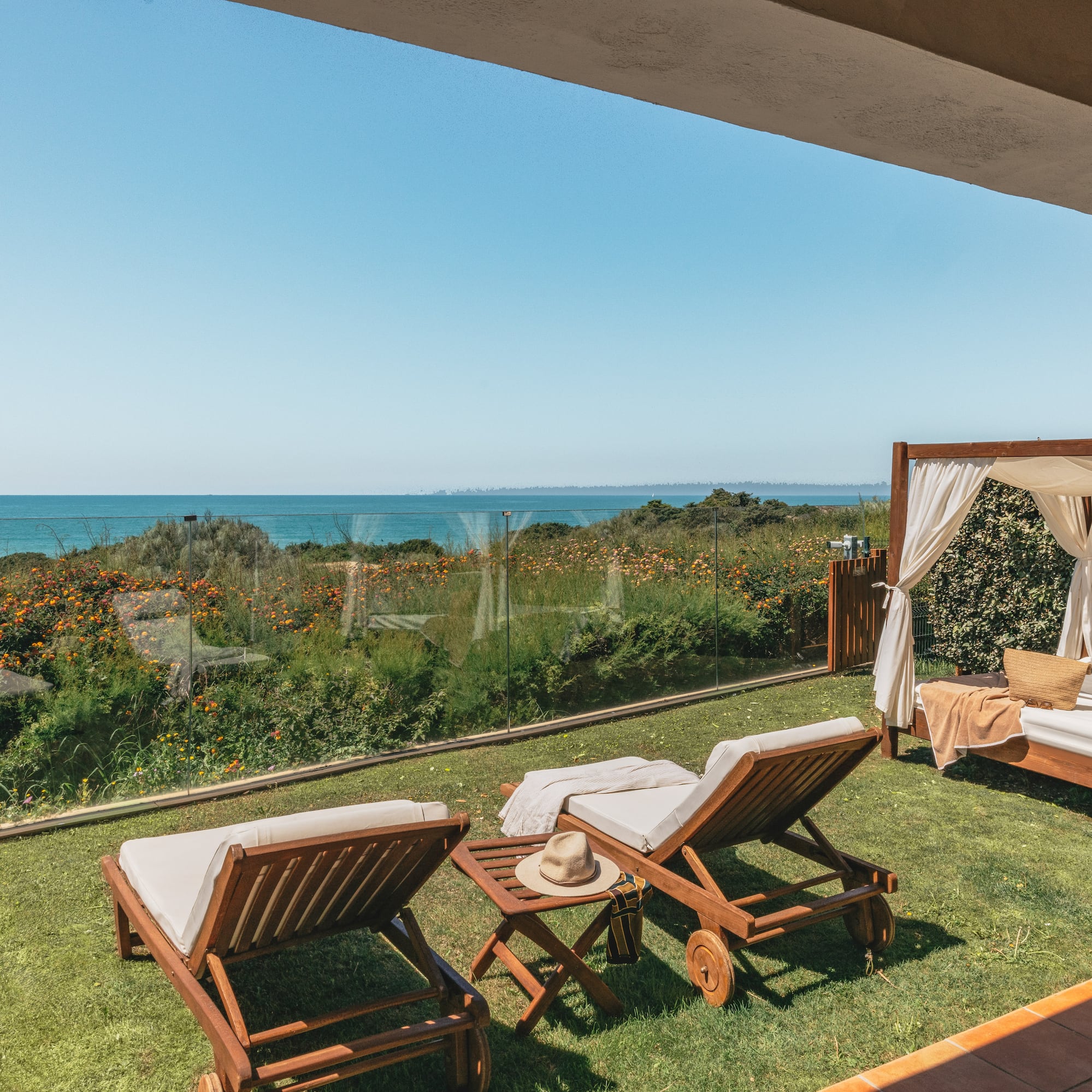 Ocean view terrace with sun loungers and cabana on a grassy lawn.