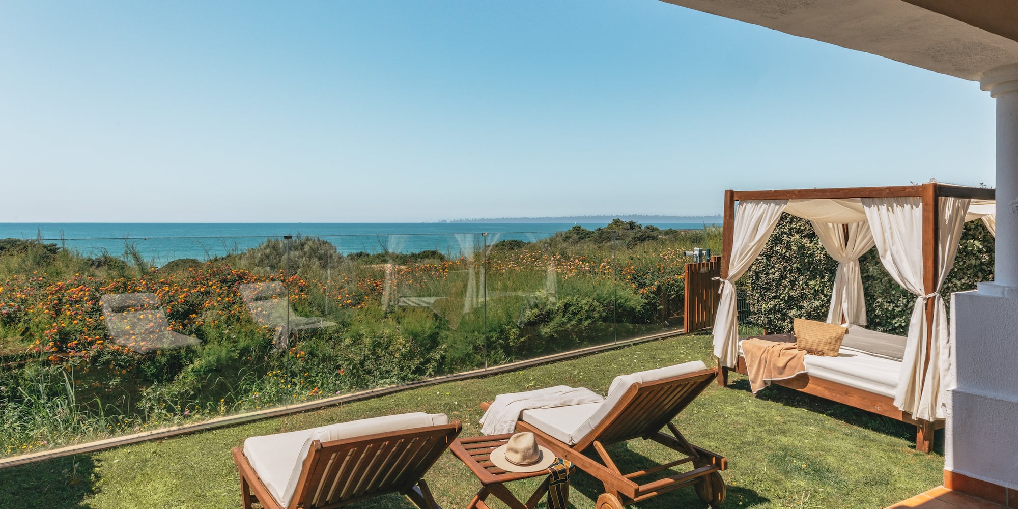 Ocean view terrace with sun loungers and cabana on a grassy lawn.