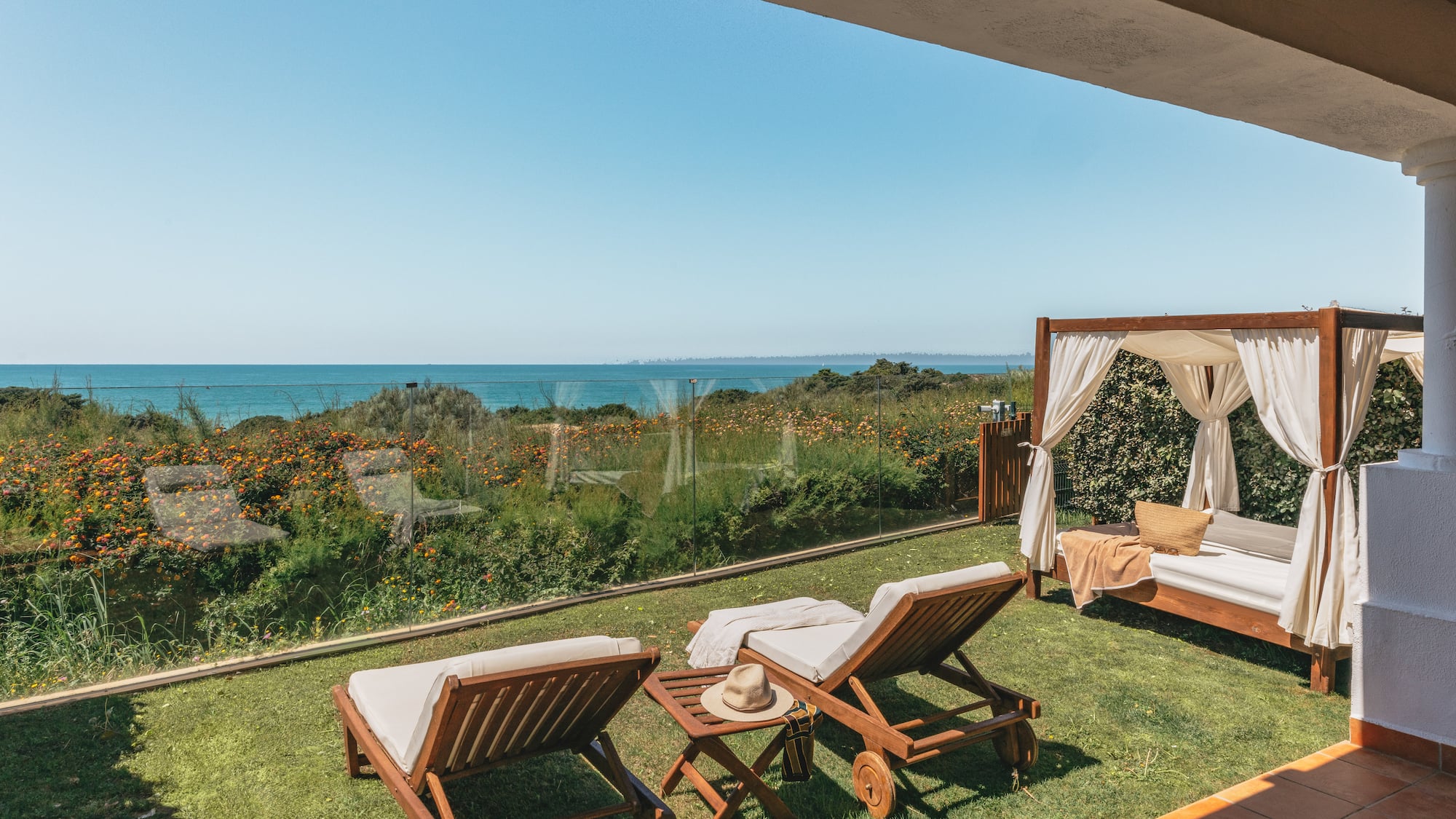 Ocean view terrace with sun loungers and cabana on a grassy lawn.