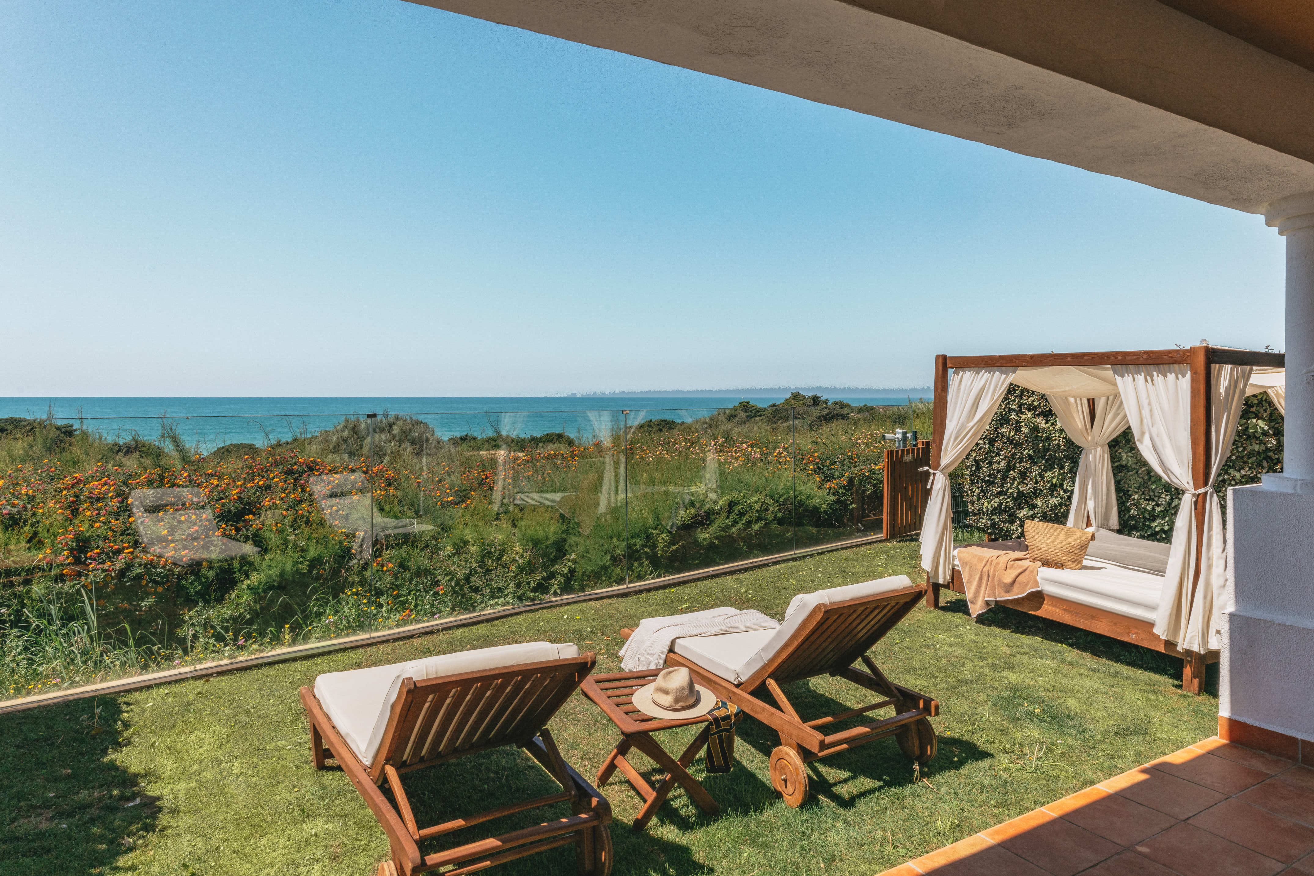 Ocean view terrace with sun loungers and cabana on a grassy lawn.