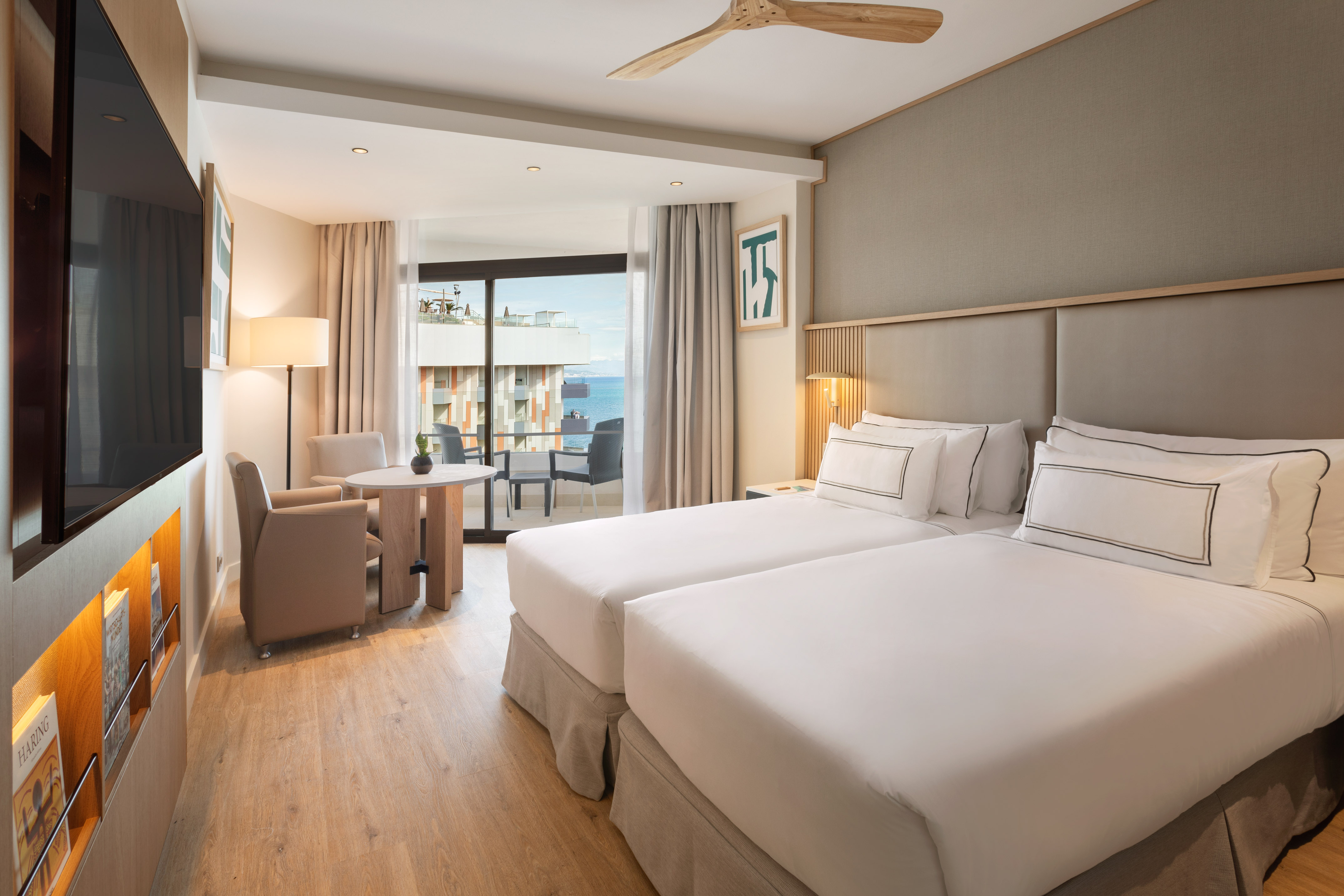 Modern hotel room with twin beds, ocean view balcony, and sitting area.