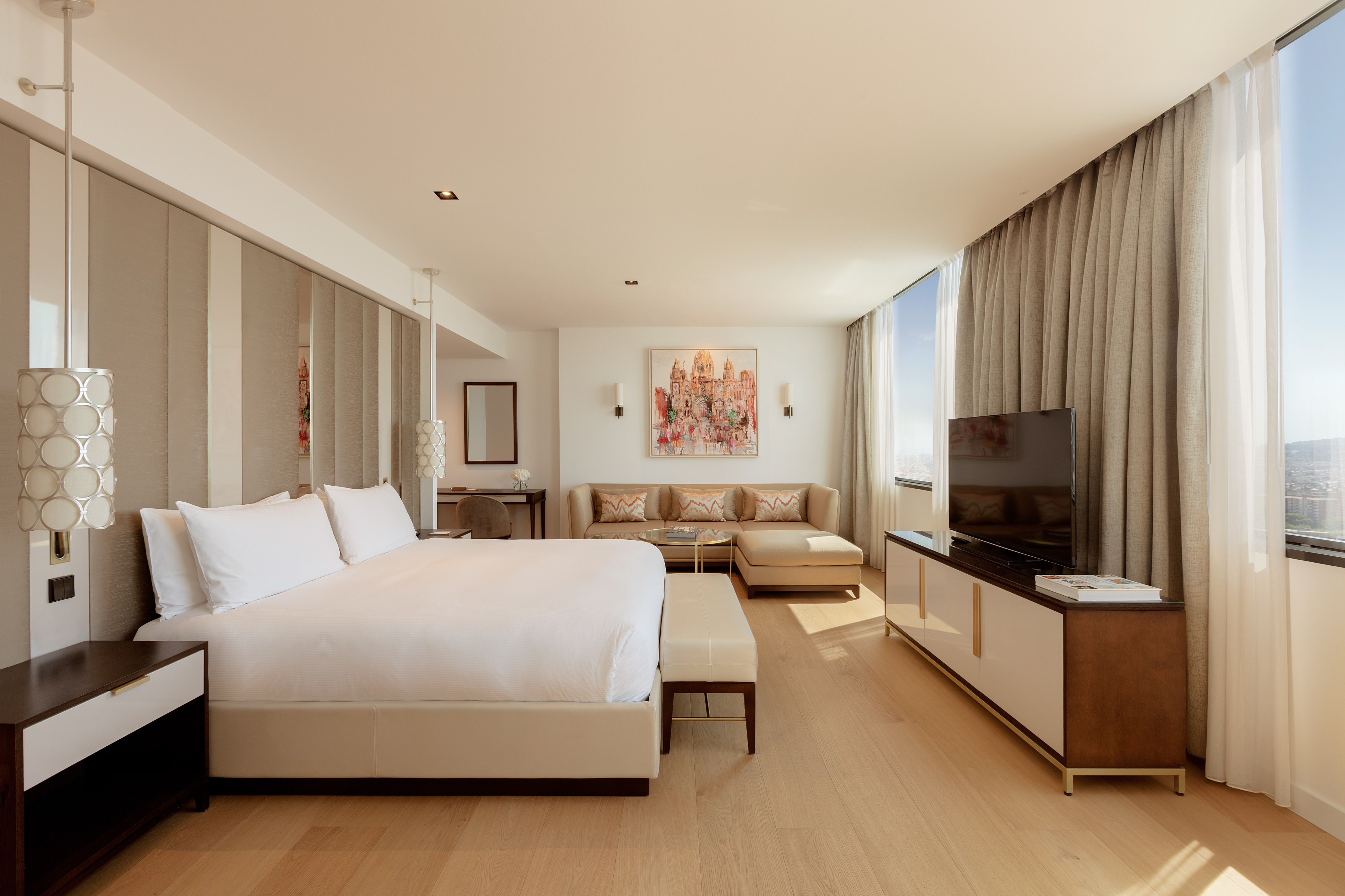 Luxury hotel suite with bed, sofa, TV console, and city view.