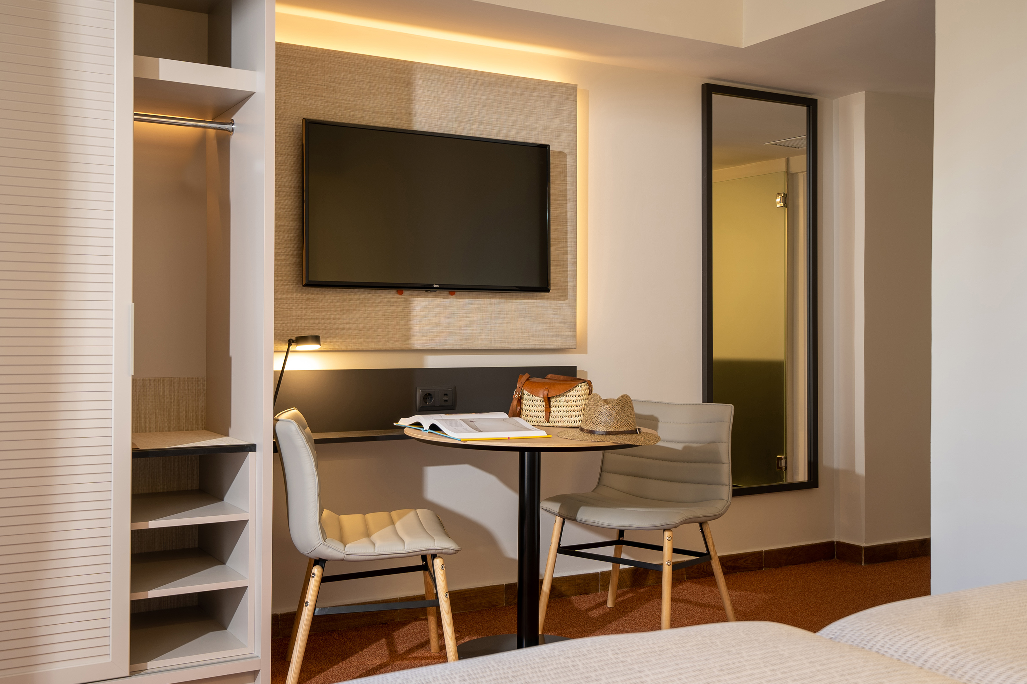 Stylish hotel room: TV, built-in wardrobe, table with chairs, and mirror.