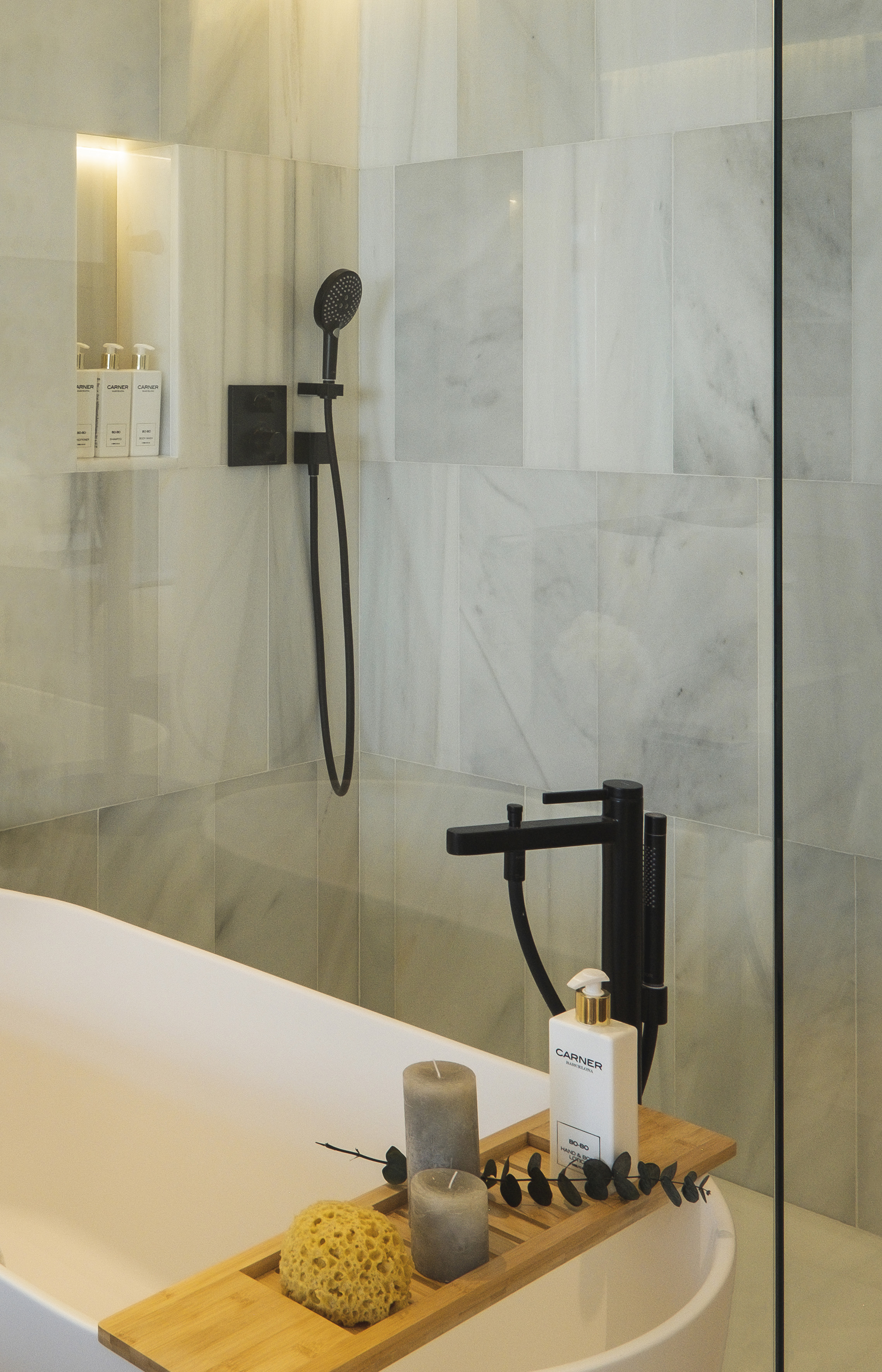 Modern marble bathroom with freestanding tub, black fixtures, and bath caddy.