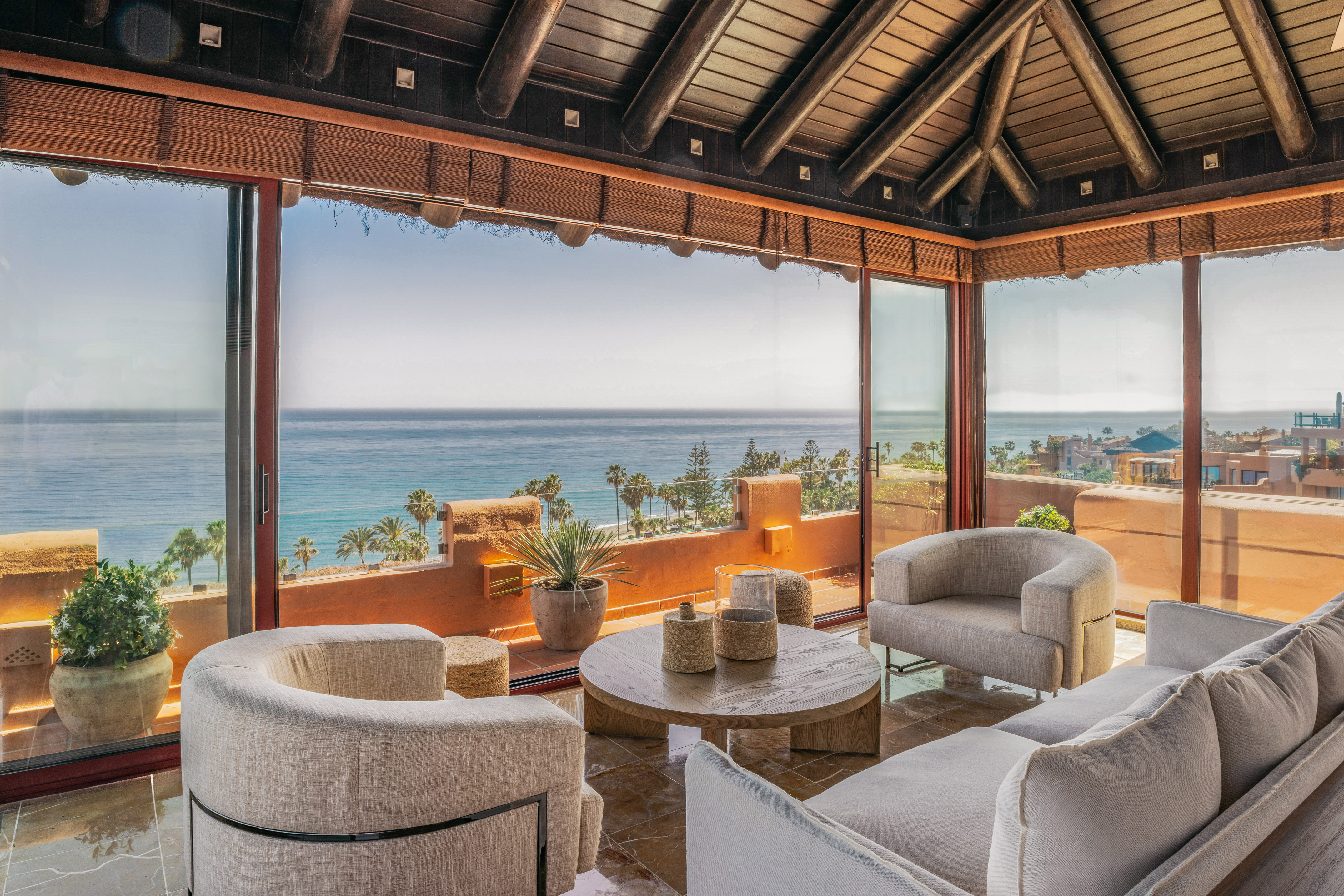 Luxury living room with ocean view, modern furniture, and wooden beamed ceiling.