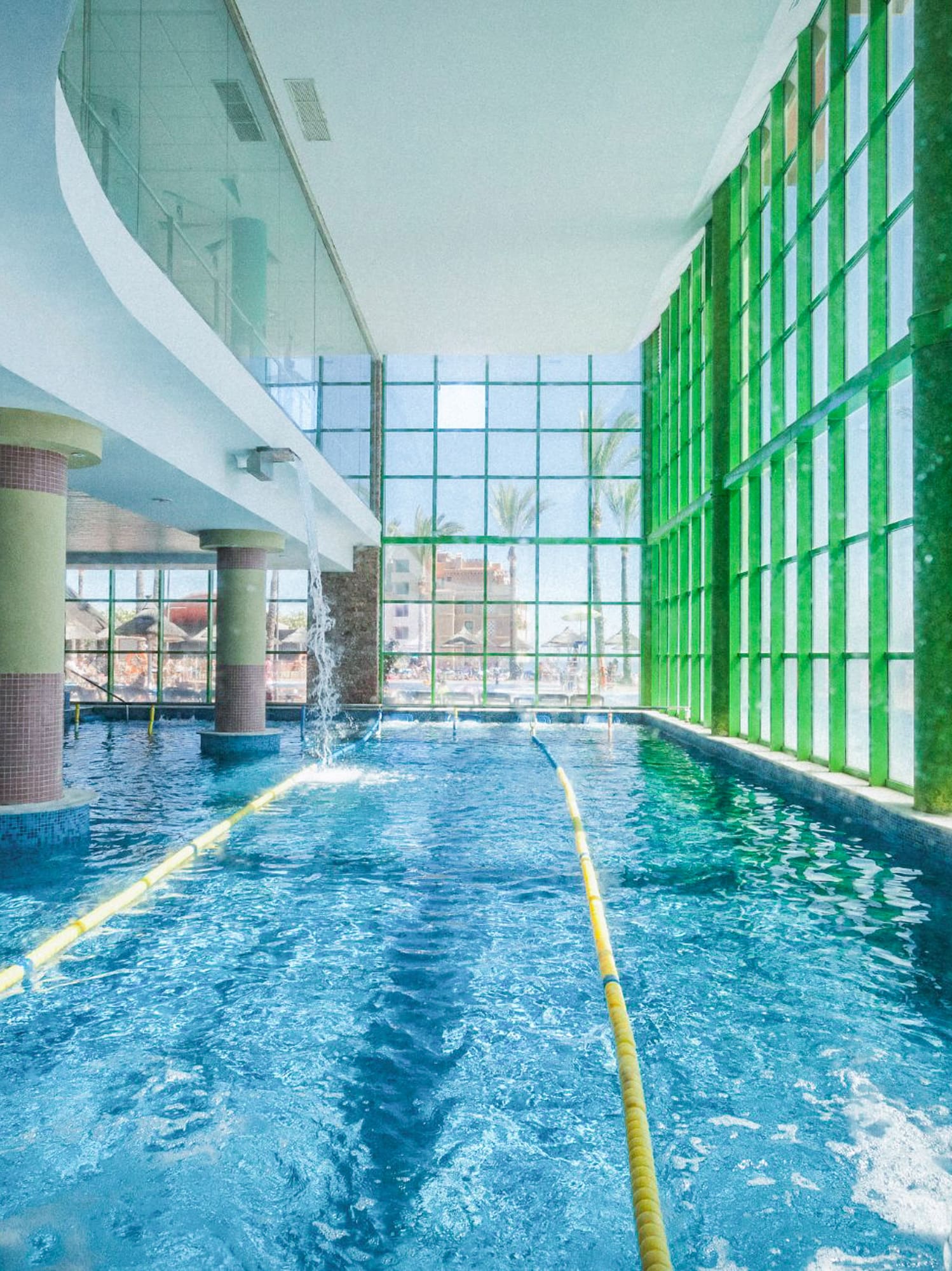 Indoor swimming pool, bright, with fountains, yellow lane, and green windows.