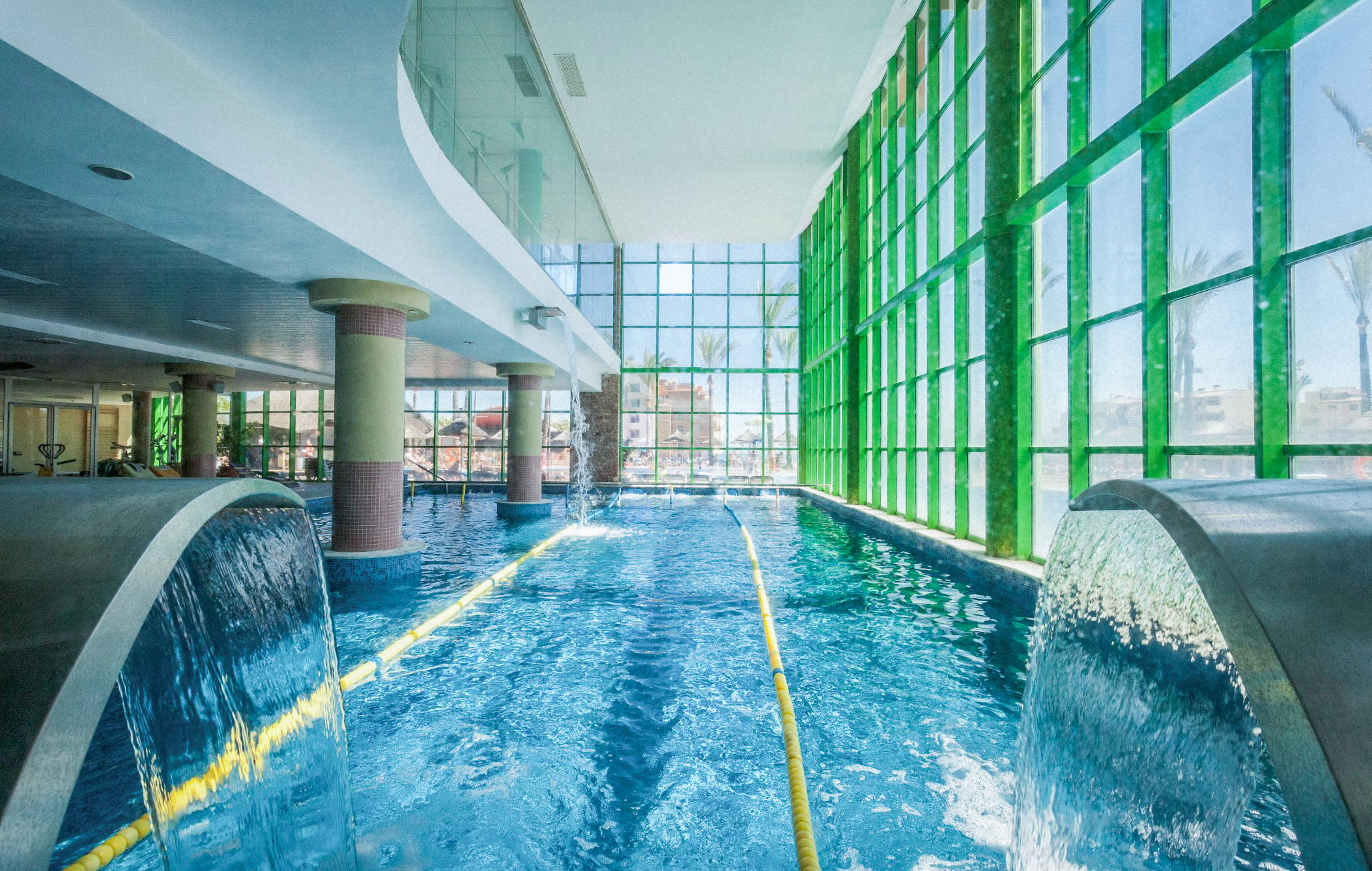 Indoor swimming pool, bright, with fountains, yellow lane, and green windows.