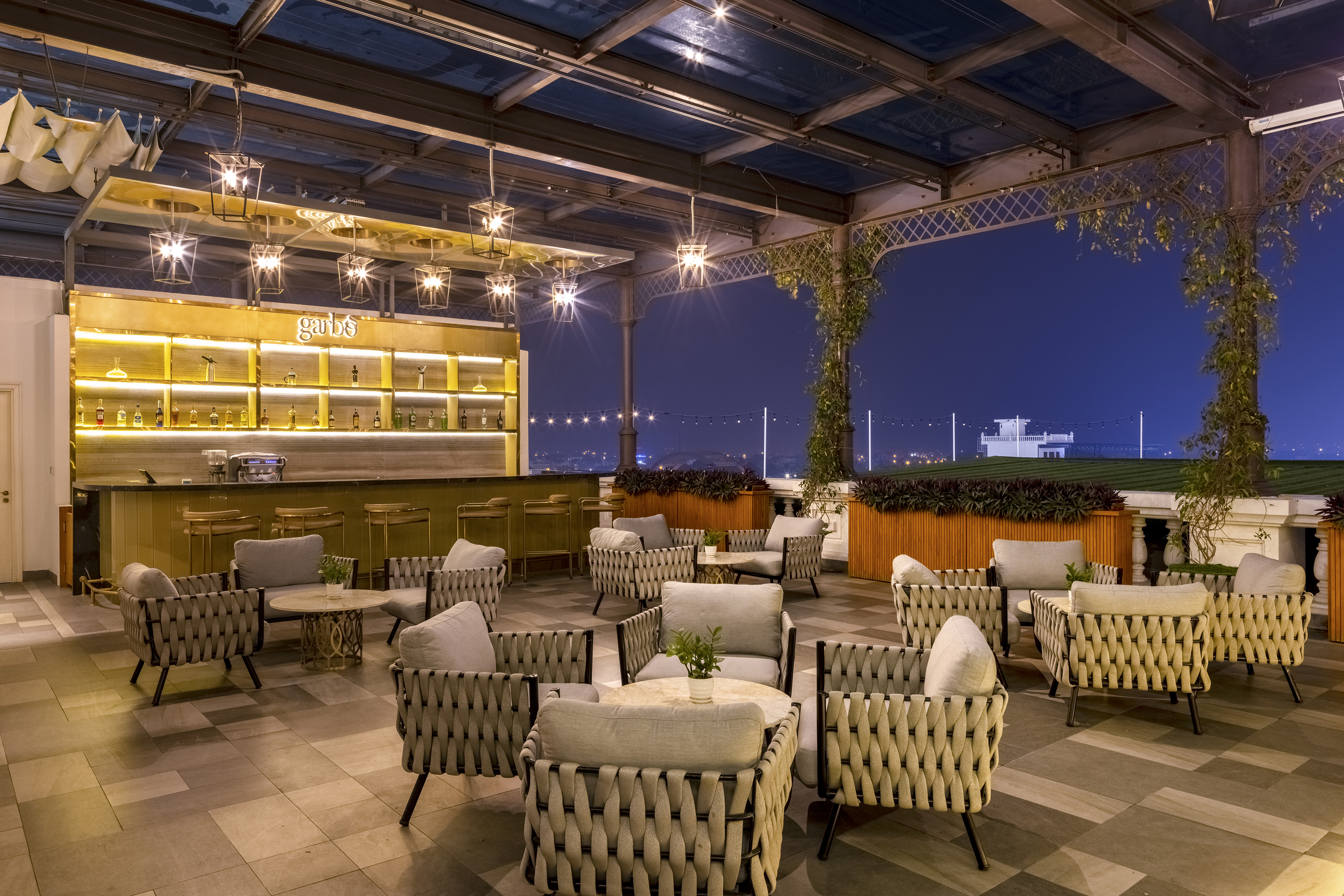 Nighttime rooftop bar with illuminated bar, stylish outdoor seating, city skyline.