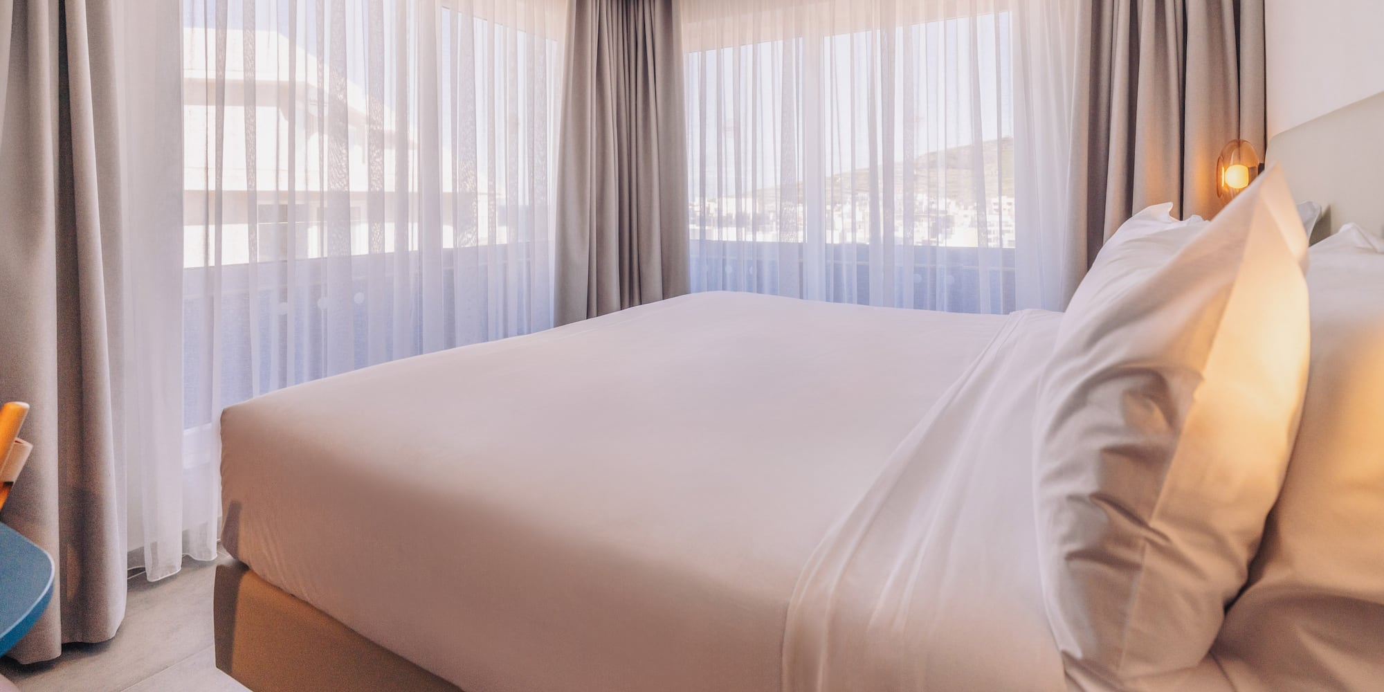 a bed with white sheets and pillows in a room with curtains