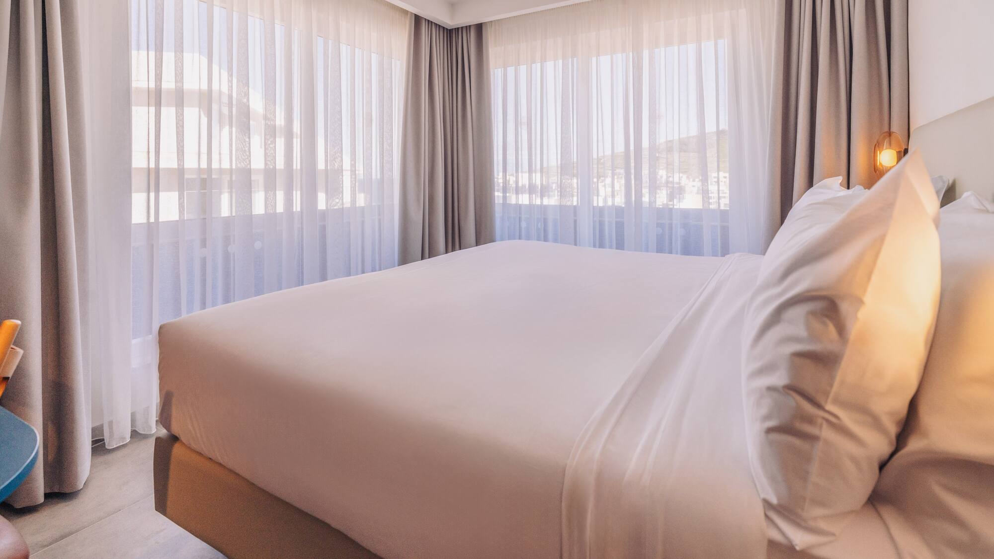 a bed with white sheets and pillows in a room with curtains