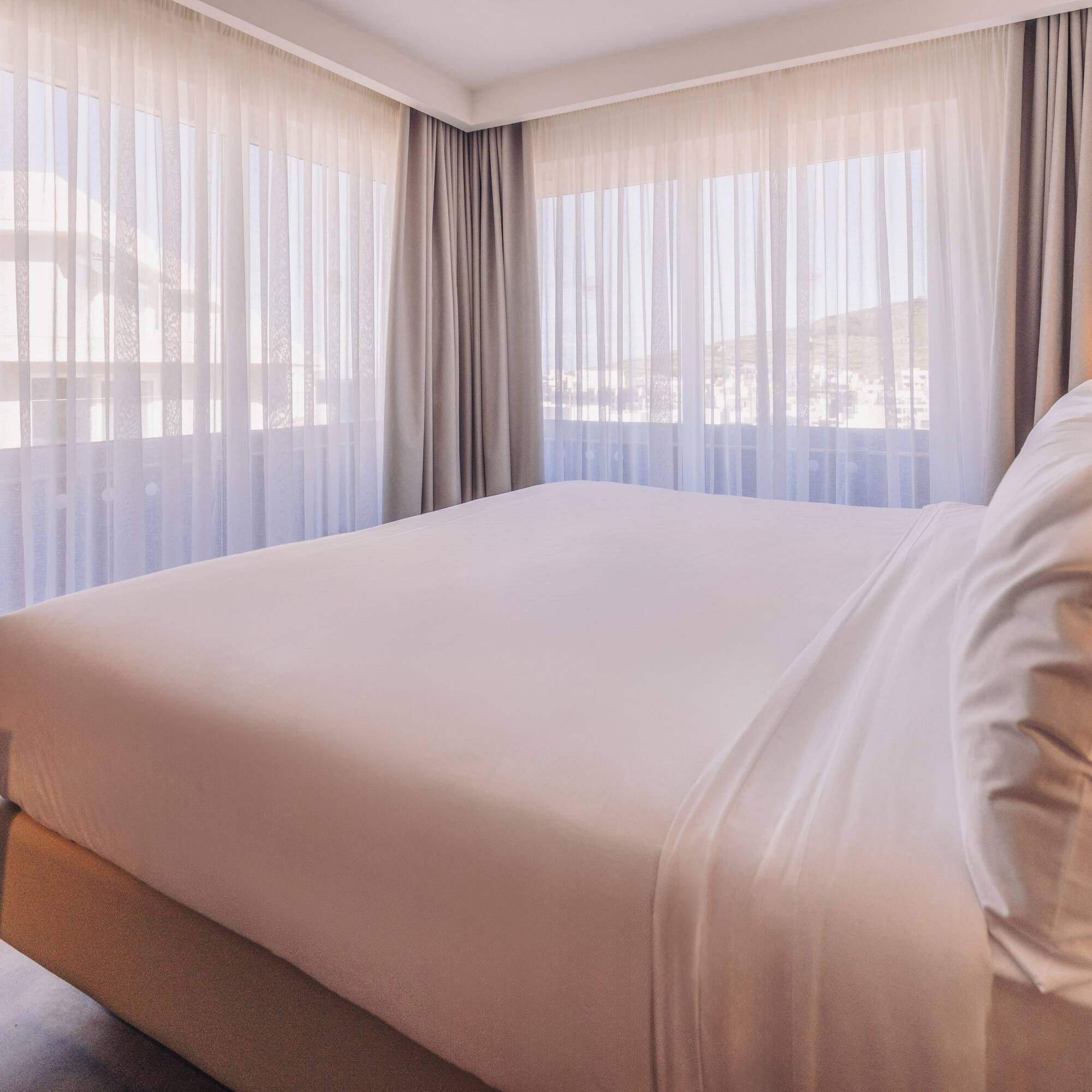 a bed with white sheets and pillows in a room with curtains